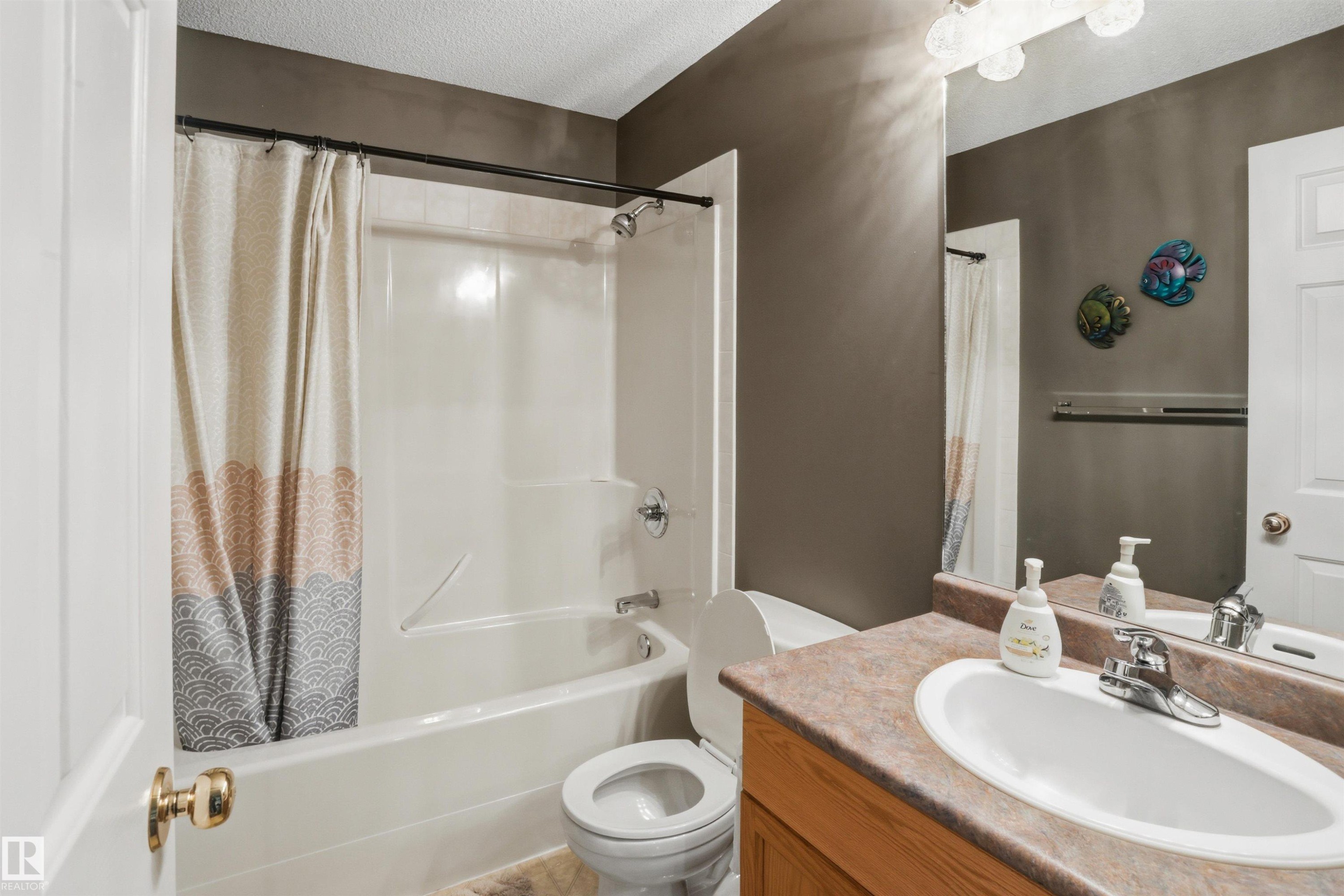Bathroom featuring a shower-over-tub combination with white surround, a toilet, and a vanity with an integrated sink and laminate countertop - 396 Kananaskis Way, Devon, AB - Indoor Photo Showing Bathroom