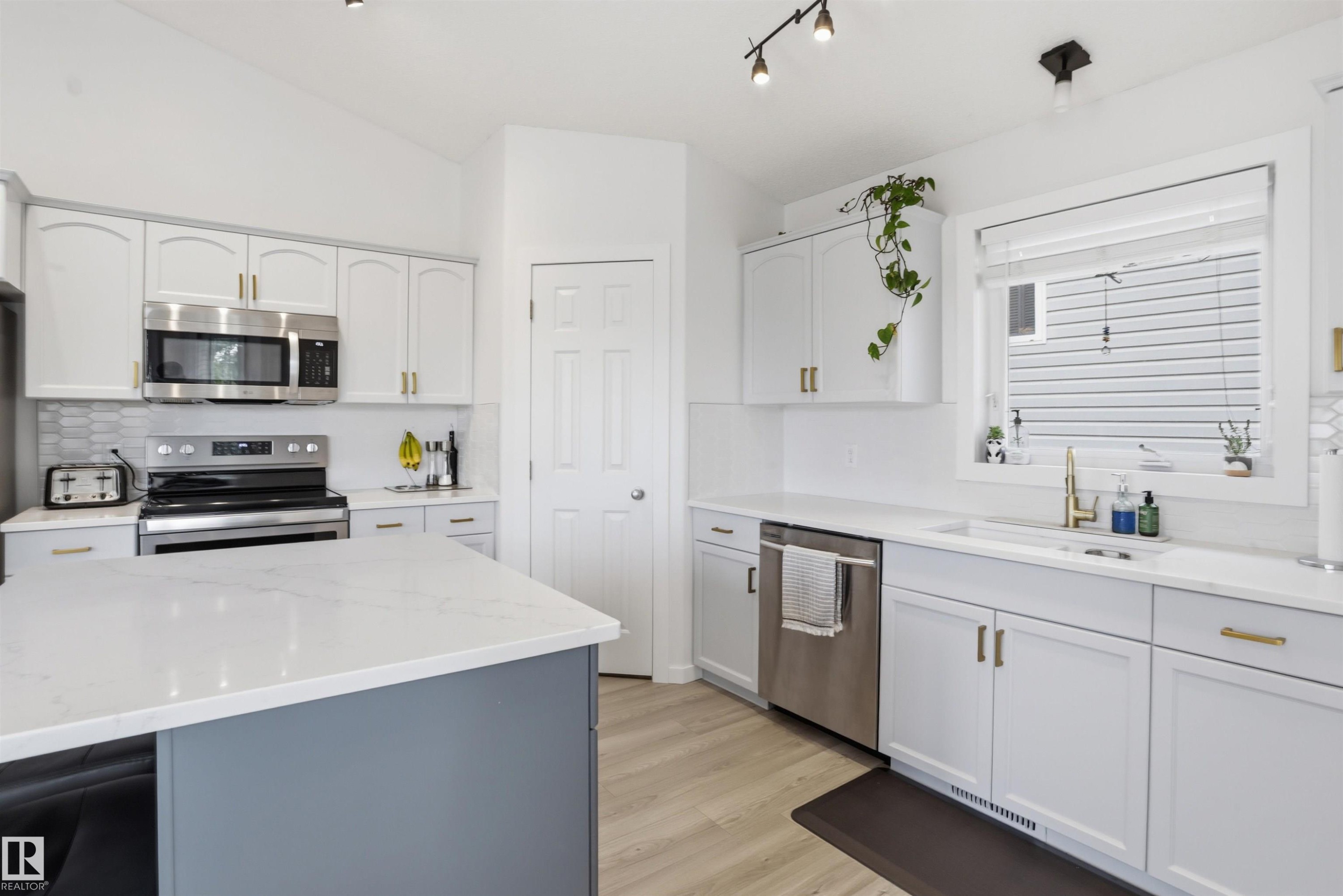 Bright kitchen featuring white cabinetry, light countertops, wood-finish flooring, a stainless steel range, and a stainless steel microwave - 396 Kananaskis Way, Devon, AB - Indoor Photo Showing Kitchen