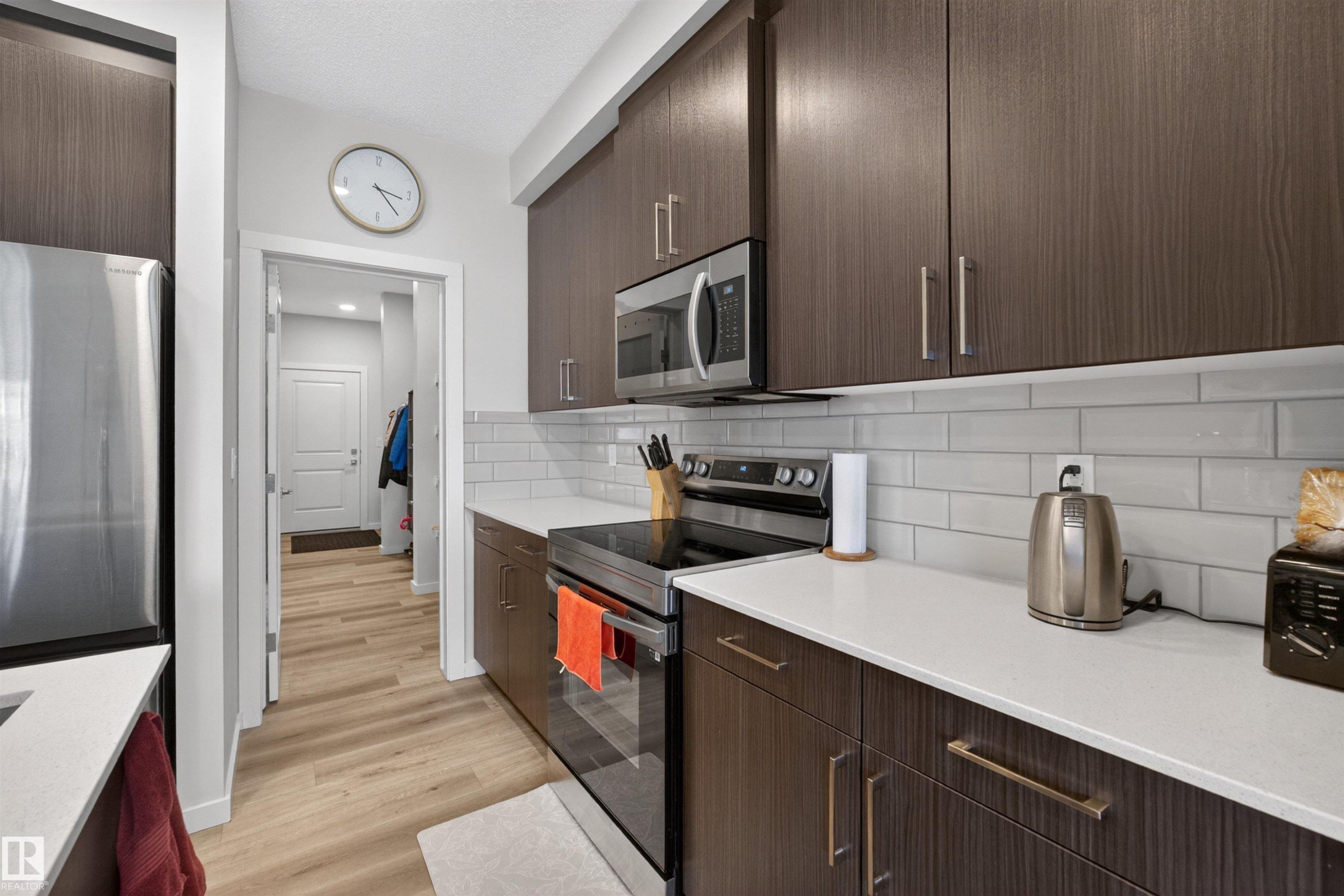 Kitchen featuring wood-finish cabinetry with modern hardware, stainless steel appliances, white subway tile backsplash, and light-toned countertops - 332 Juniper Cove, Leduc, AB - Indoor Photo Showing Kitchen With Upgraded Kitchen