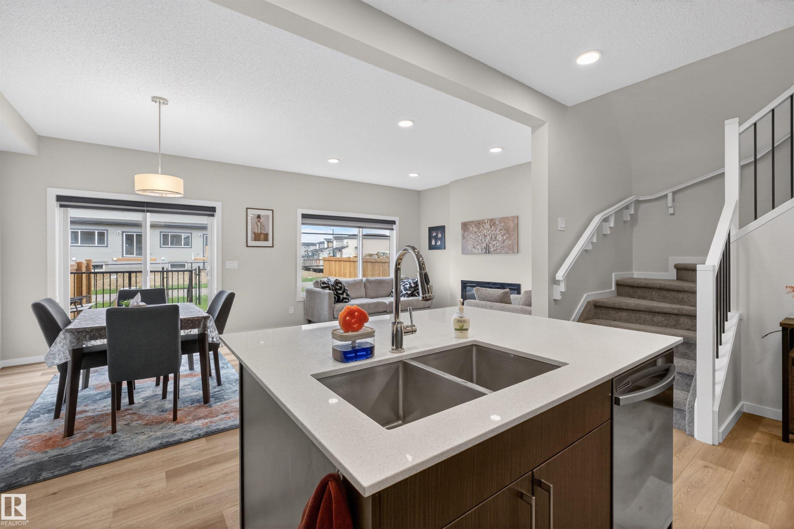 Kitchen island with a double stainless steel sink, a stainless steel dishwasher, and a light-toned countertop - 332 Juniper Cove, Leduc, AB - Indoor