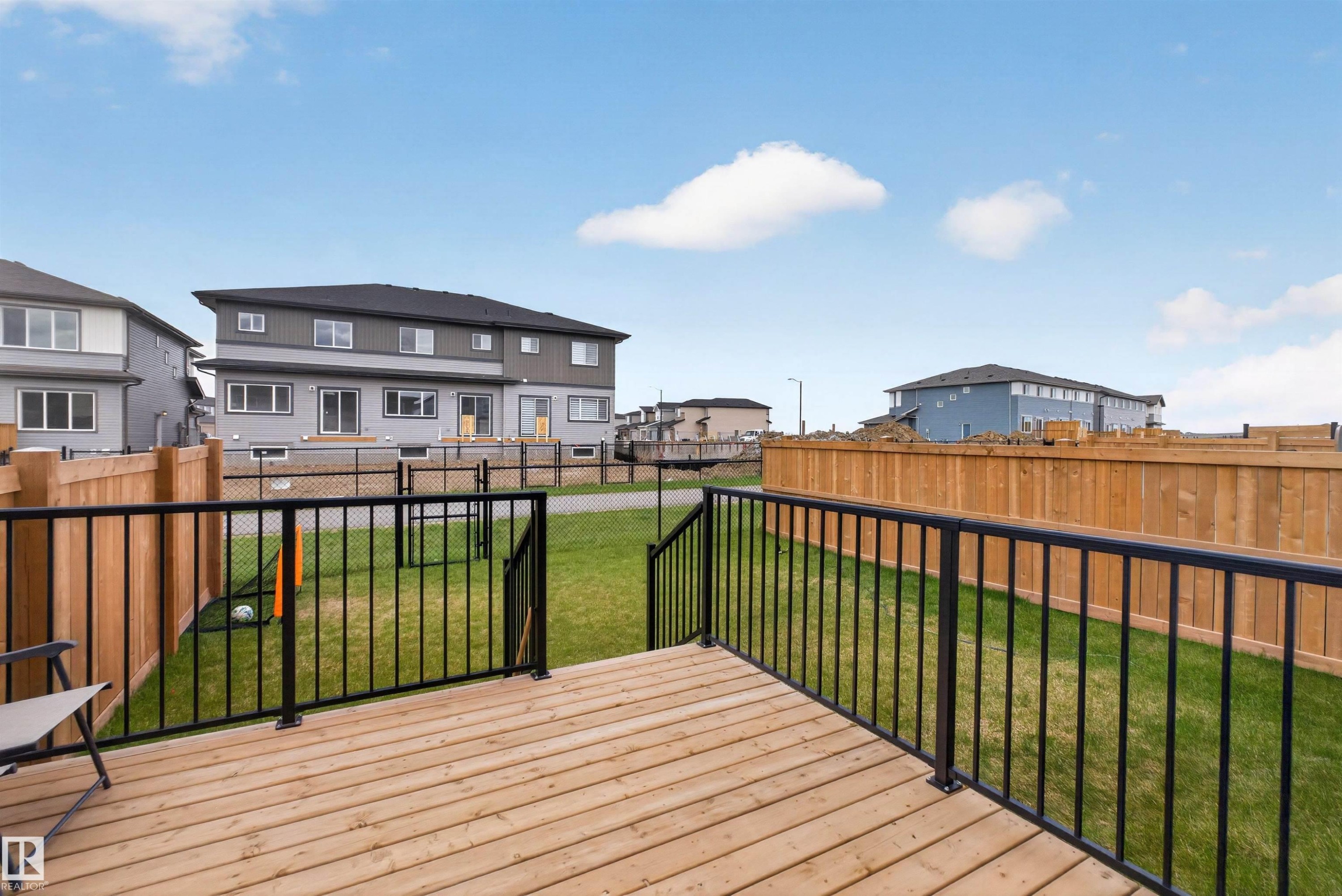 Spacious wood deck with black metal railings overlooking a backyard with green grass and a wood fence - 332 Juniper Cove, Leduc, AB - Outdoor With Deck Patio Veranda With Exterior