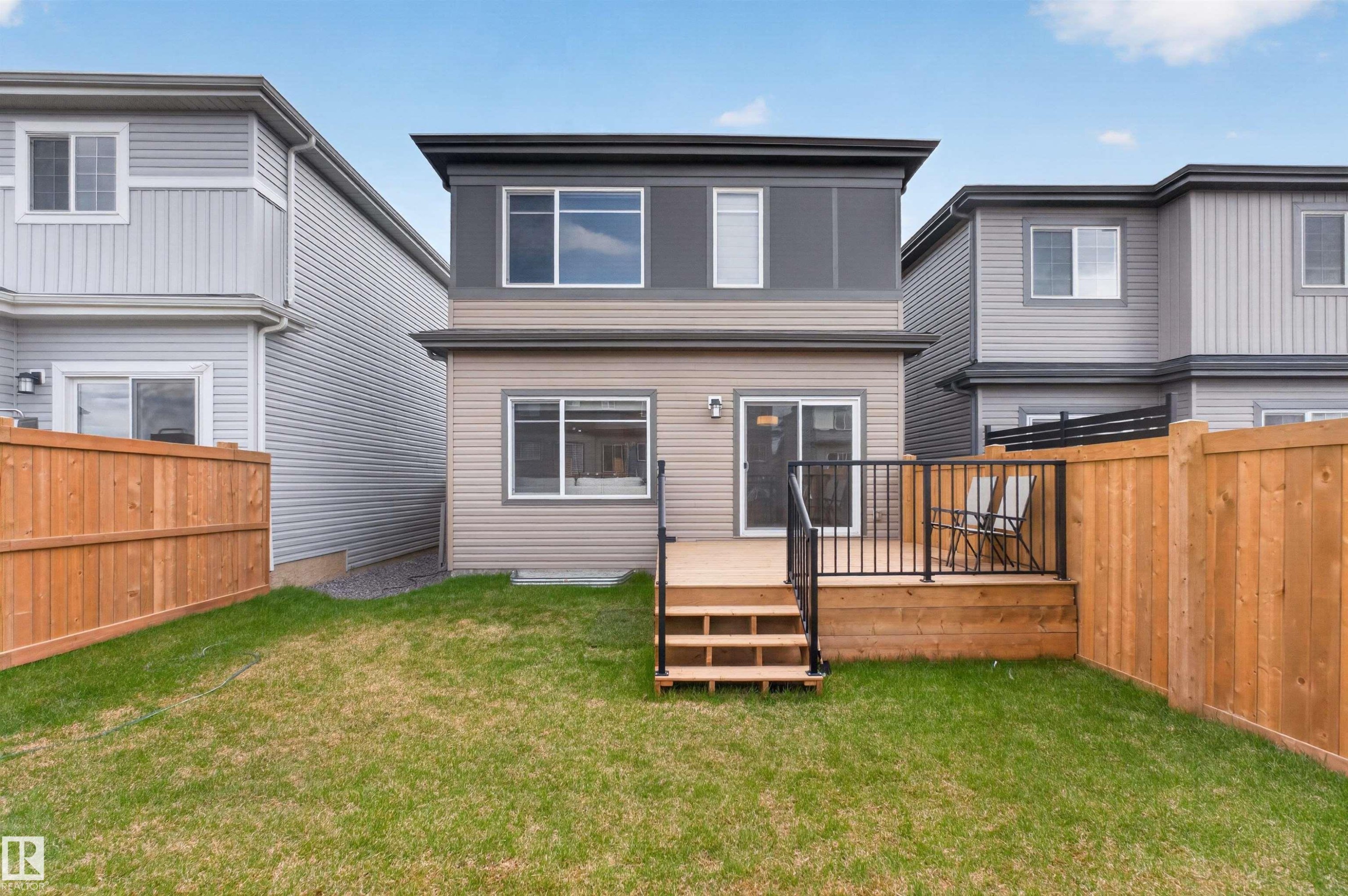 Rear exterior featuring a two-story design with a neutral siding facade and dark trim accents - 332 Juniper Cove, Leduc, AB - Outdoor