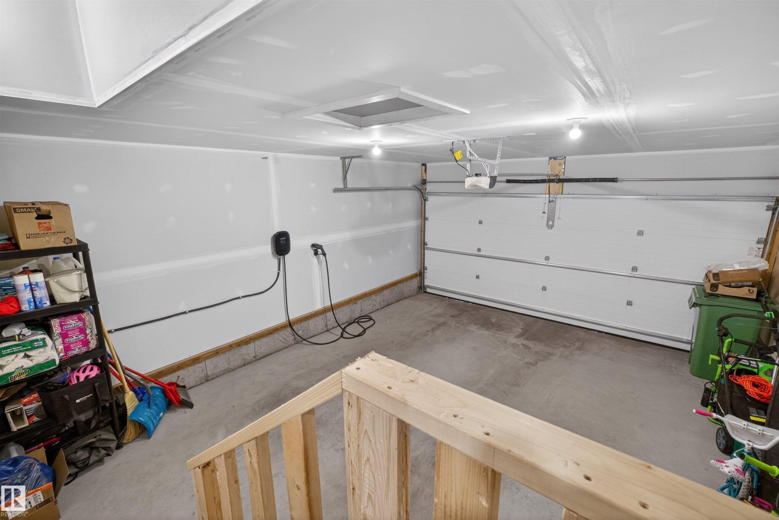 Attached garage space featuring a white sectional garage door, concrete flooring, and an electric vehicle charging station - 332 Juniper Cove, Leduc, AB - Indoor Photo Showing Garage
