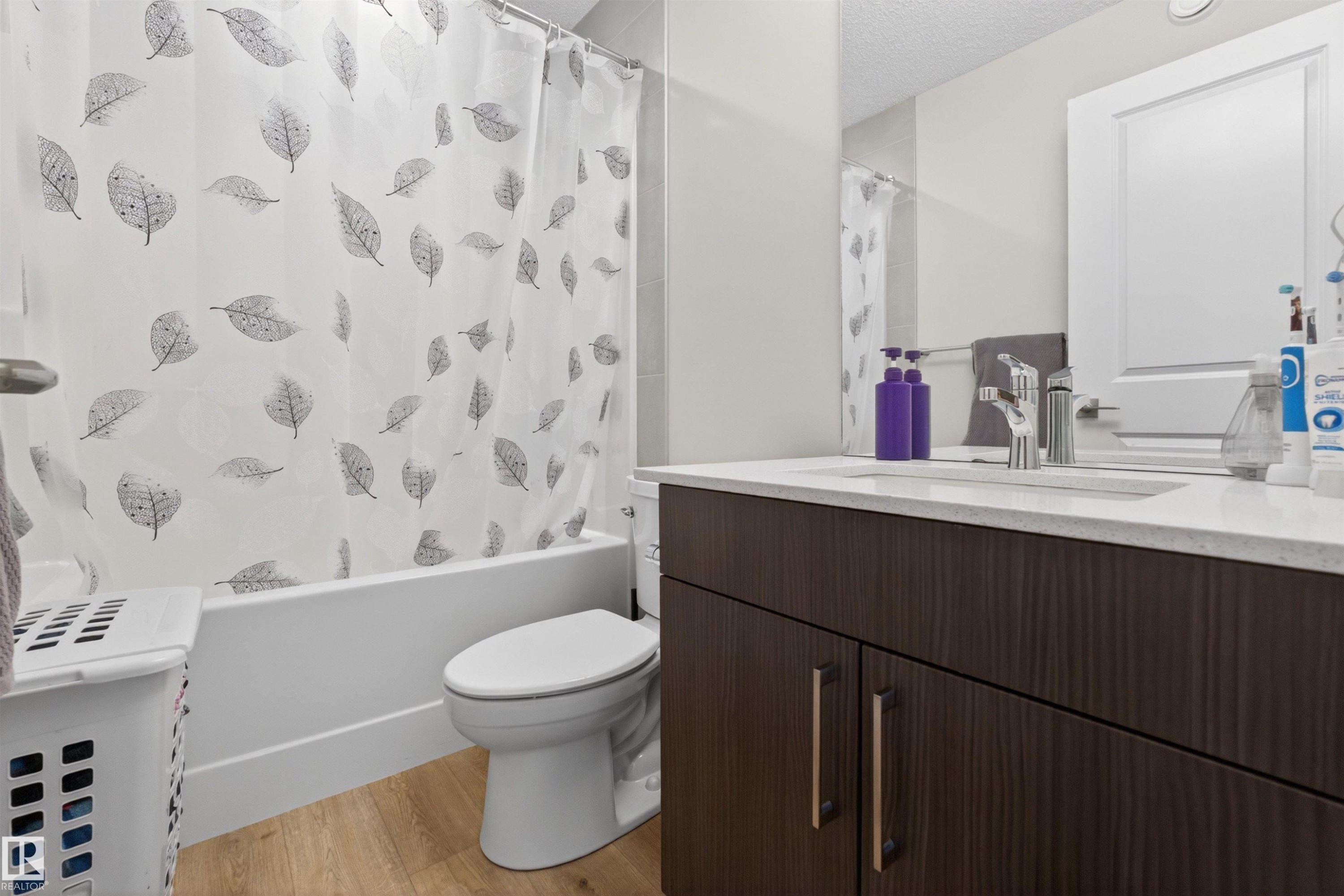 Bathroom featuring a dark wood-finish vanity with a light countertop, an integrated sink with a chrome faucet, a white toilet, and a white bathtub with a shower - 332 Juniper Cove, Leduc, AB - Indoor Photo Showing Bathroom