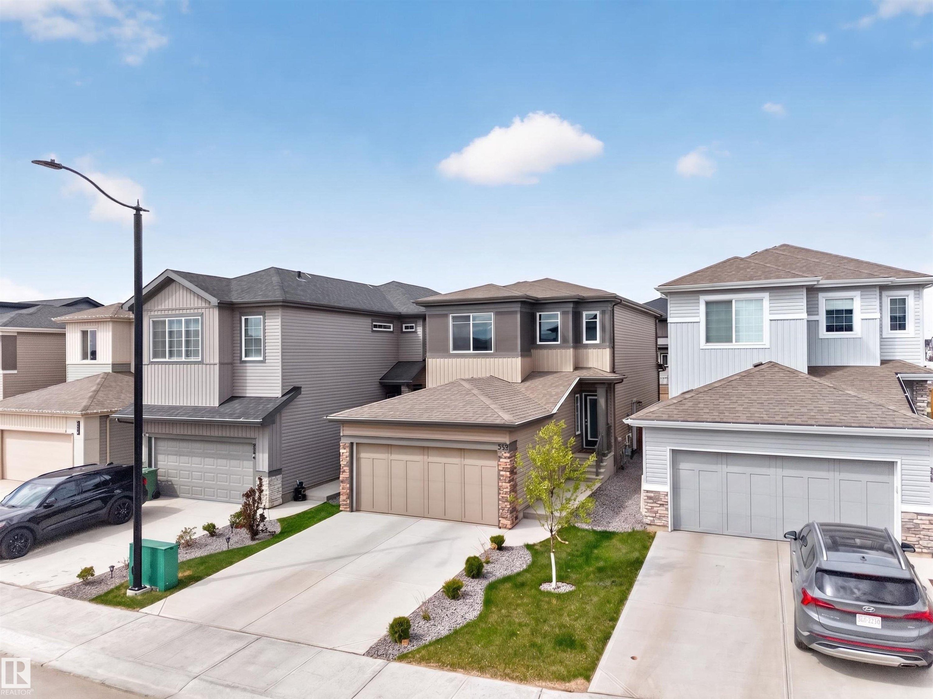 Contemporary two-story residence featuring a two-car garage, stone veneer accents, and a landscaped front yard - 332 Juniper Cove, Leduc, AB - Outdoor With Facade