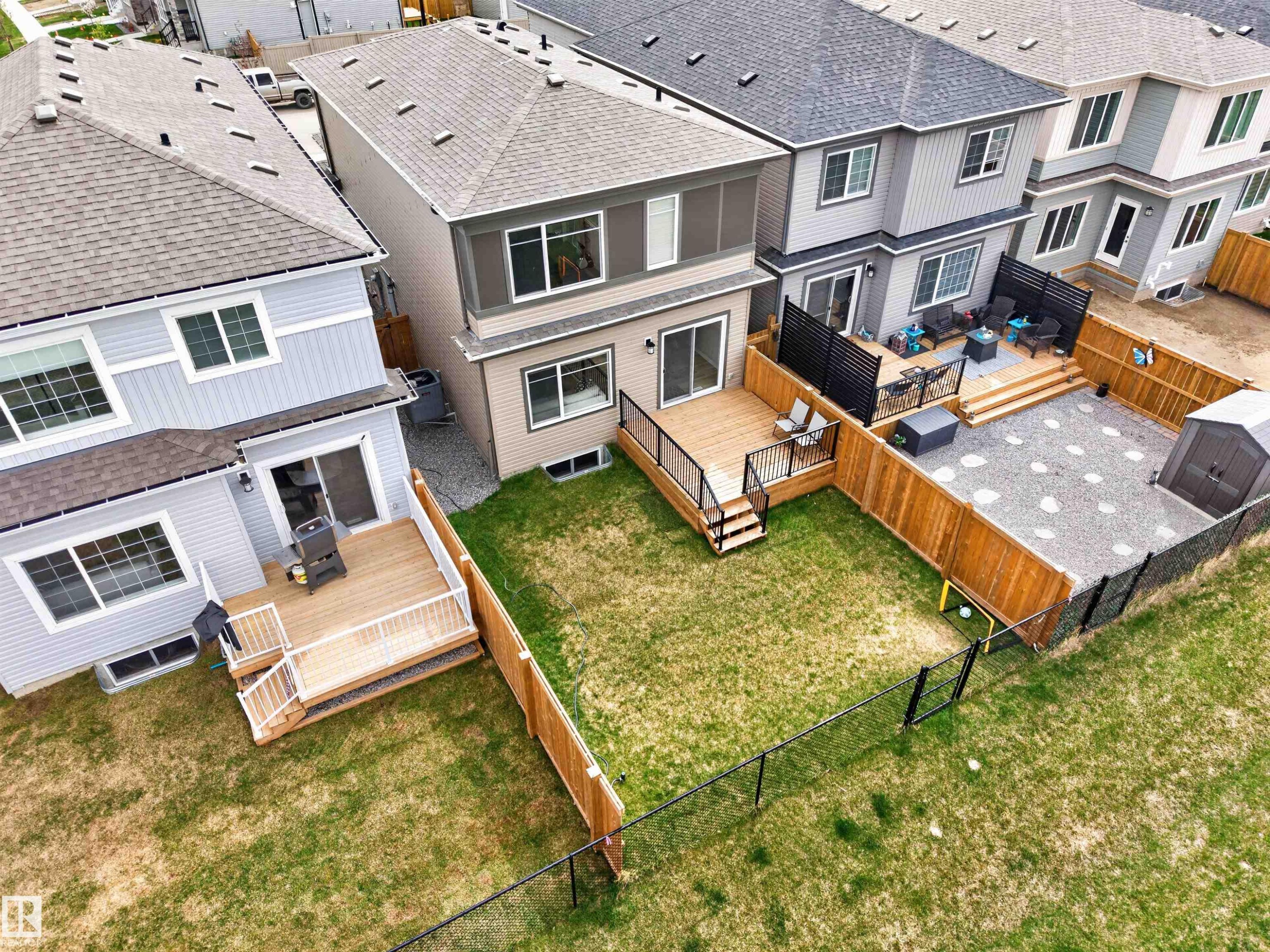 Expansive backyard featuring a manicured lawn, multi-level wood deck with black railings, and a gravel patio with stepping stones - 332 Juniper Cove, Leduc, AB - Outdoor With Deck Patio Veranda