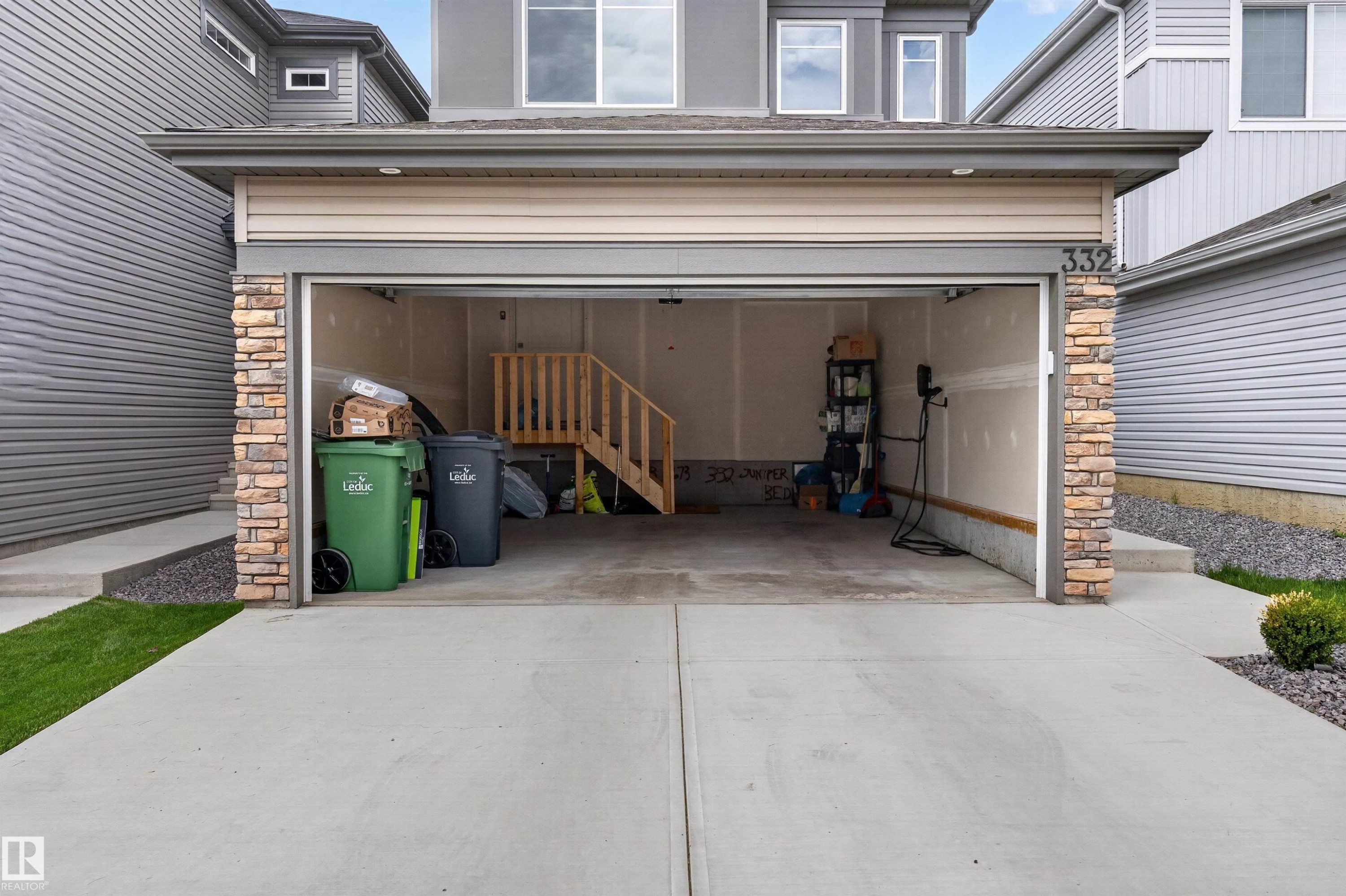 Attached two-car garage featuring a concrete driveway and stacked stone accents on the facade - 332 Juniper Cove, Leduc, AB - Outdoor With Exterior