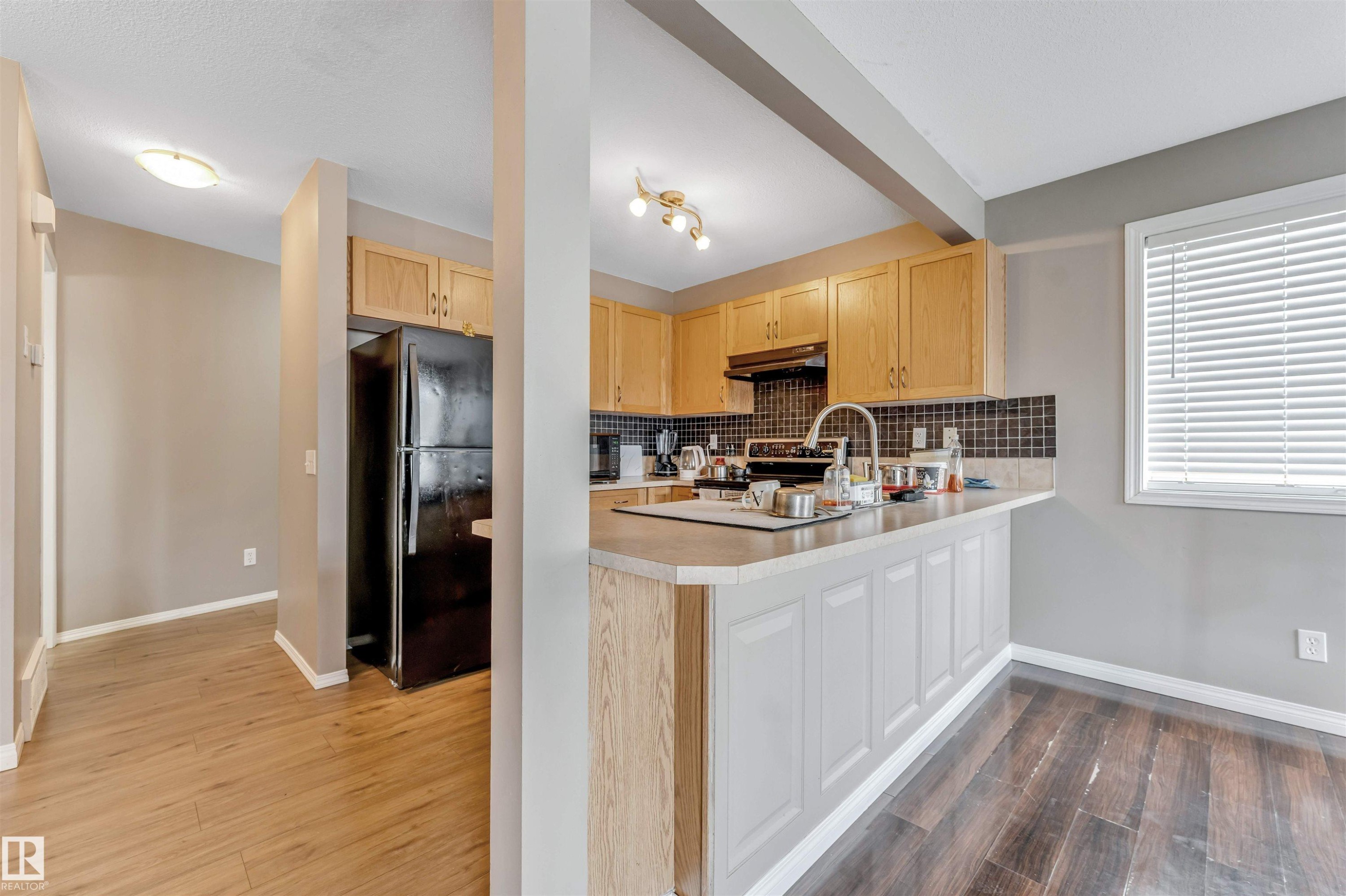 Kitchen featuring light wood cabinetry, black tiled backsplash, and a black refrigerator - 135 150 Edwards Drive, Edmonton, AB - Indoor Photo Showing Kitchen