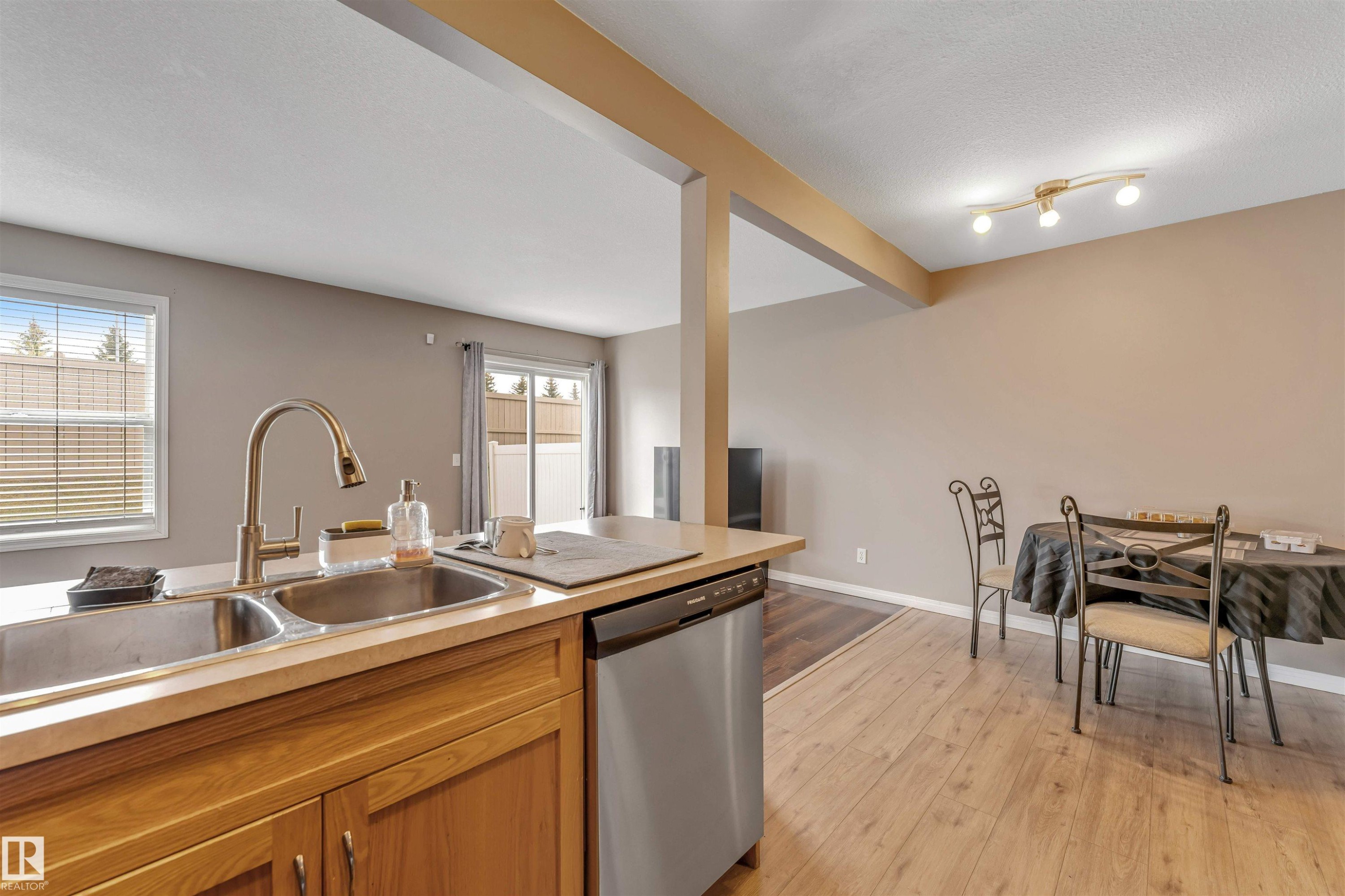 Kitchen featuring a double stainless steel sink with a high-arc faucet, light wood-finish cabinetry, and a built-in dishwasher - 135 150 Edwards Drive, Edmonton, AB - Indoor Photo Showing Kitchen With Double Sink