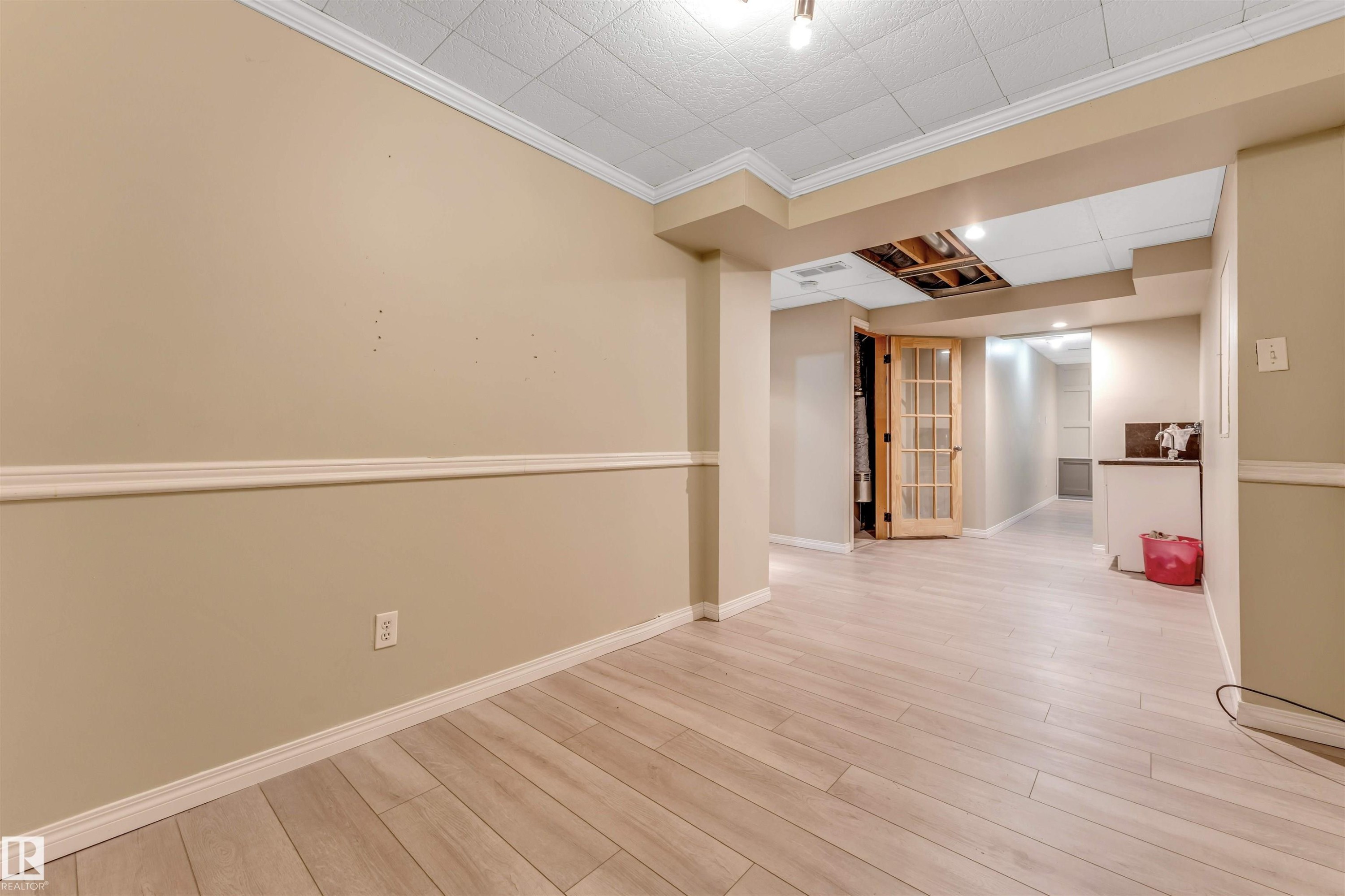 Lower level featuring wood-finish flooring, neutral wall tones, decorative chair rail molding, and a grid pattern drop ceiling - 135 150 Edwards Drive, Edmonton, AB - Indoor