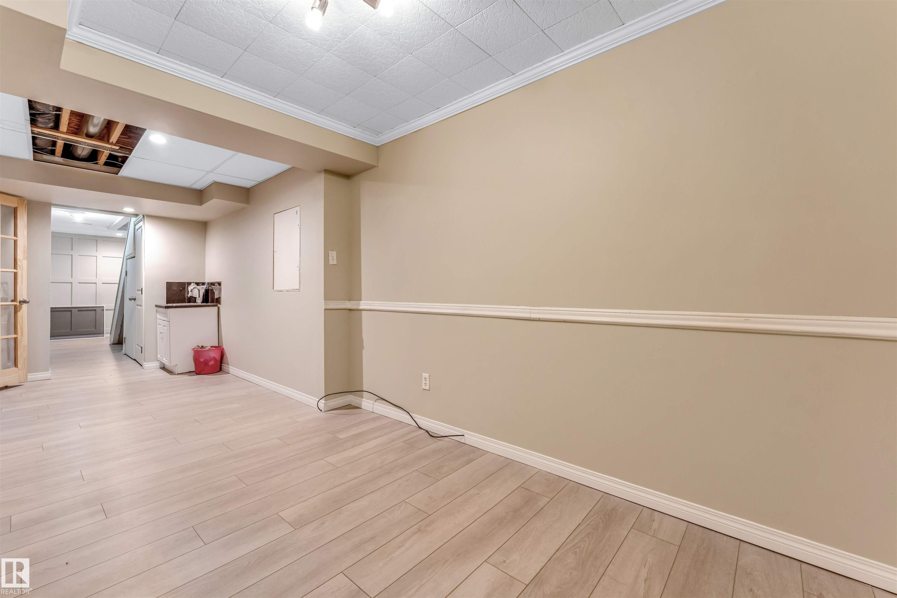 Spacious room featuring wood-finish flooring, neutral-toned walls with chair rail molding, and a drop ceiling - 135 150 Edwards Drive, Edmonton, AB - Indoor