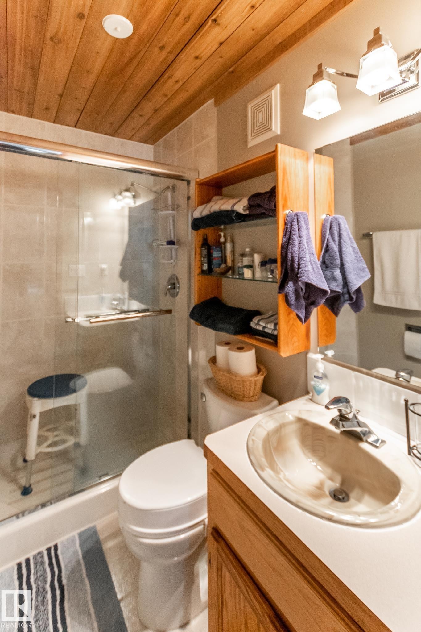 Bathroom featuring a wood-panel ceiling, tiled shower with glass enclosure, single vanity with integrated sink, wood-finish cabinetry, and wall-mounted light fixture - 4611 Lakeshore Drive, Bonnyville Town, AB - Indoor Photo Showing Bathroom