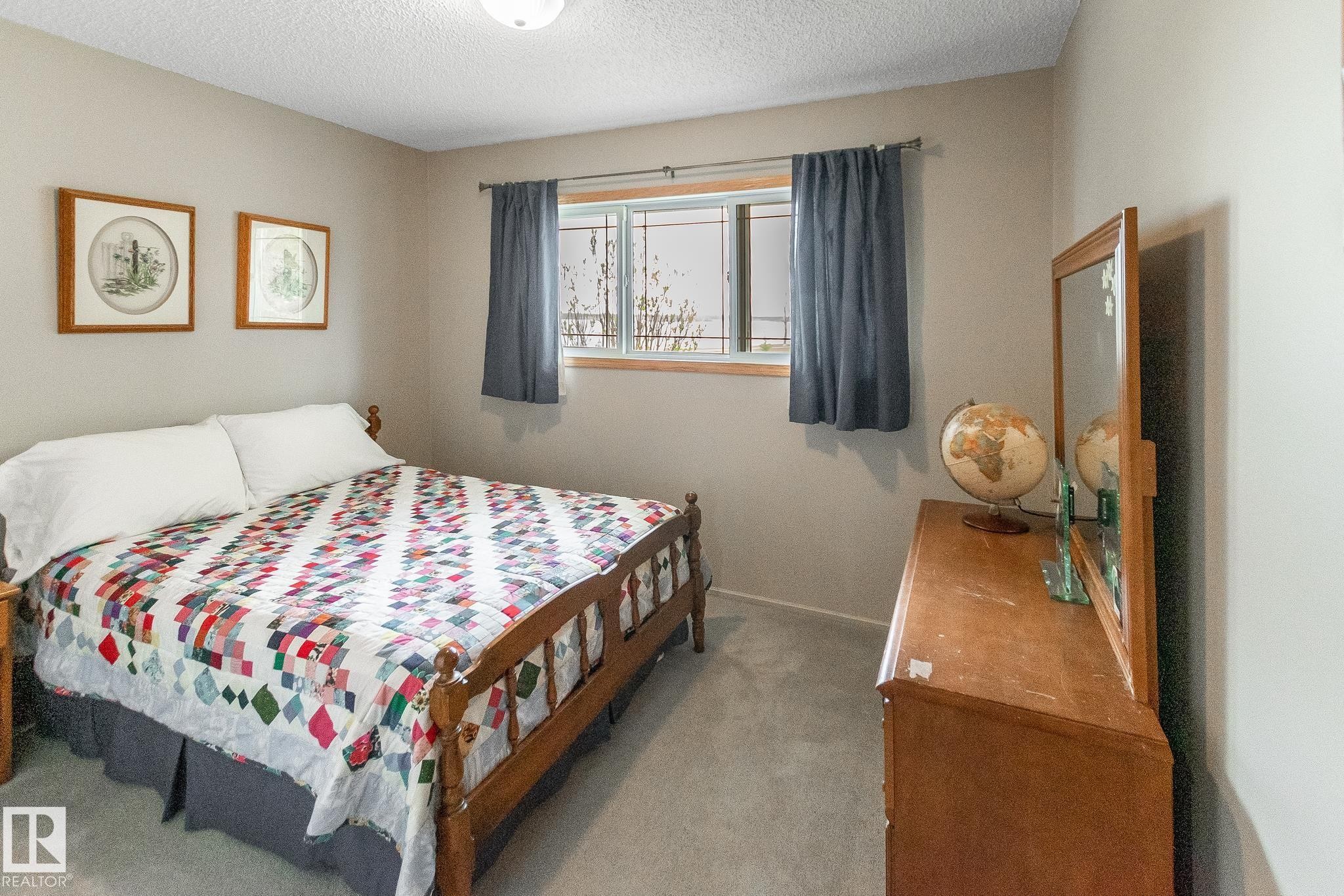 Carpeted room featuring neutral wall paint, a window with wood-finish trim, and a ceiling light fixture - 4611 Lakeshore Drive, Bonnyville Town, AB - Indoor Photo Showing Bedroom