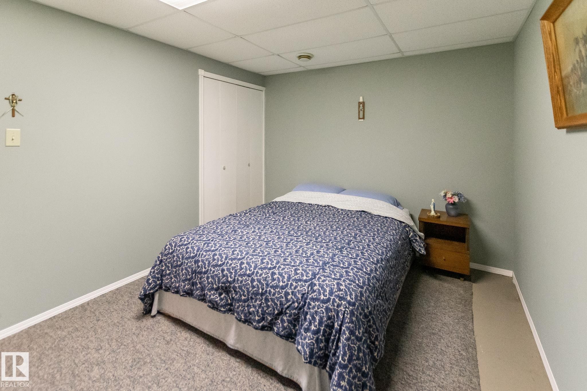 Spacious room featuring neutral wall paint, light-colored carpeting, a drop ceiling, and bi-fold closet doors - 4611 Lakeshore Drive, Bonnyville Town, AB - Indoor Photo Showing Bedroom