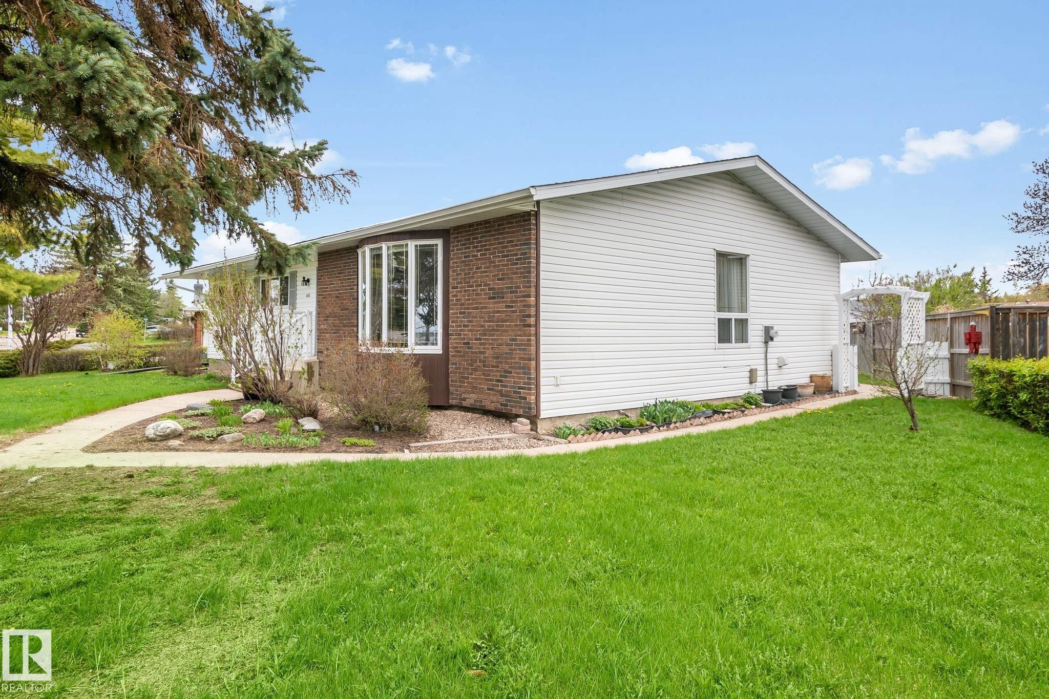 Exterior featuring brick and white siding, a bay window, a concrete walkway, mature trees, and a grassy lawn - 4611 Lakeshore Drive, Bonnyville Town, AB - Outdoor