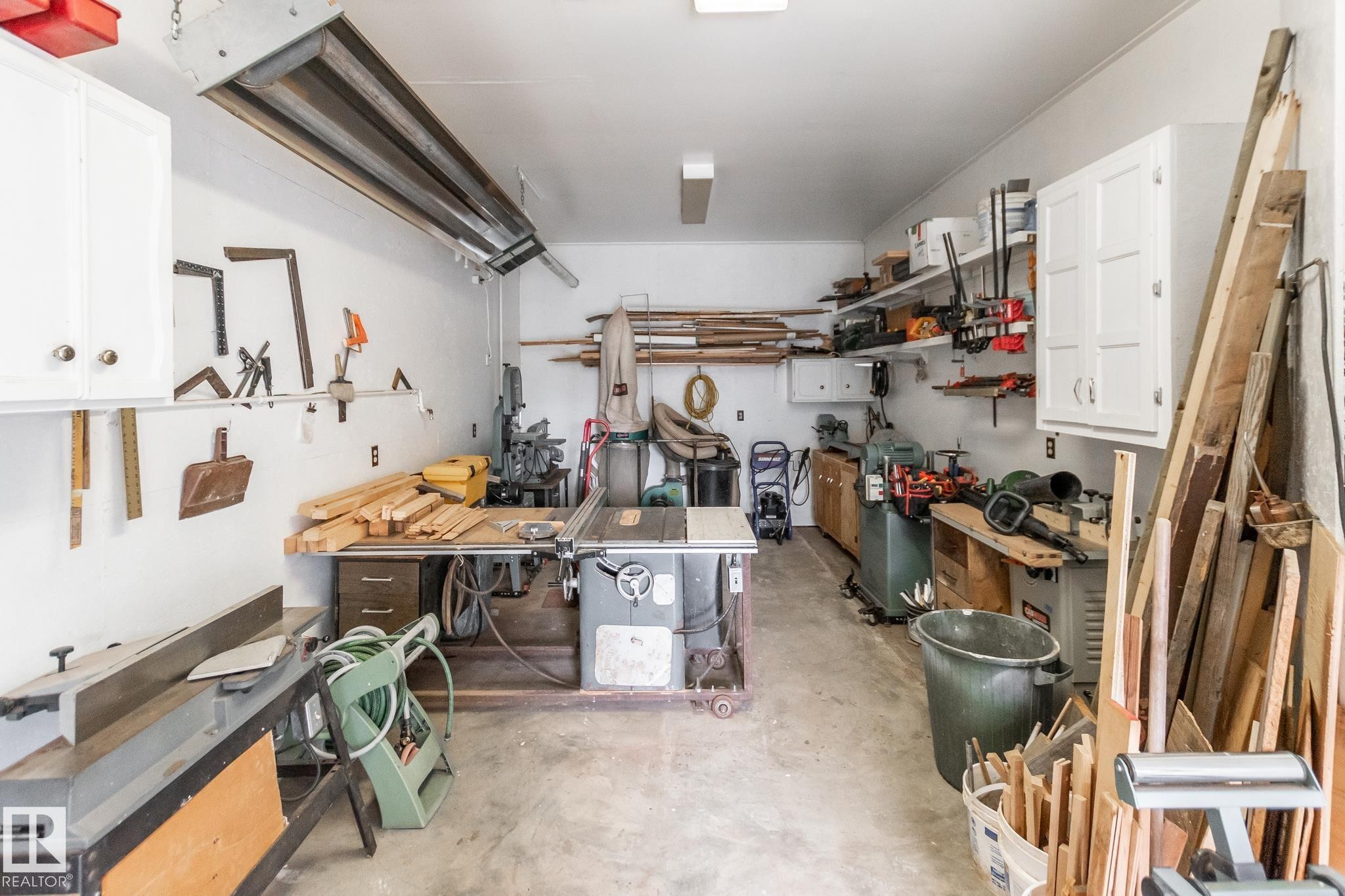 Spacious garage featuring a concrete floor, overhead lighting, wall-mounted cabinetry, and open shelving for organized storage - 4611 Lakeshore Drive, Bonnyville Town, AB - Indoor