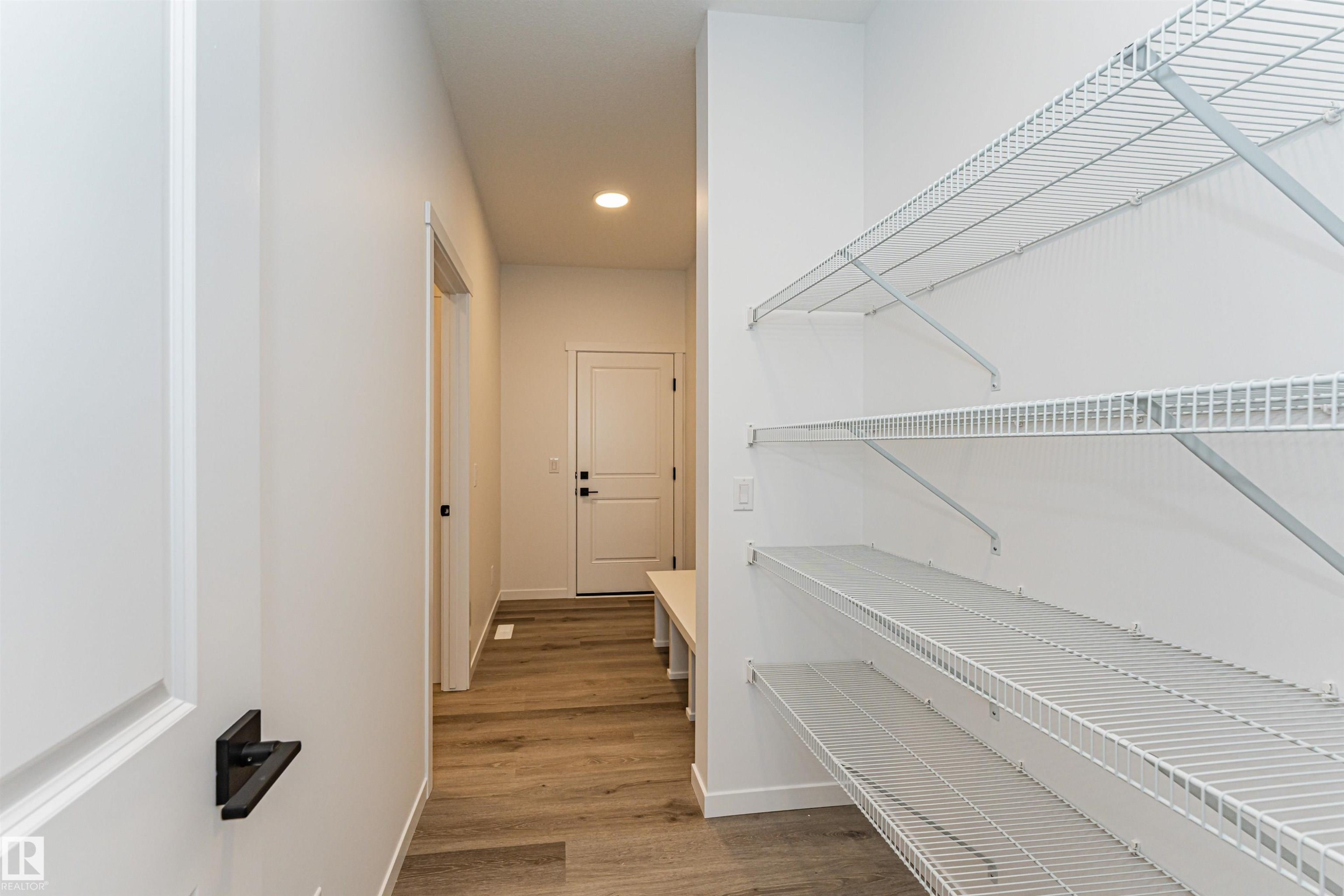 This entry area features wood-effect flooring and a white door with black hardware, leading to a space with wire shelving - 2355 Egret Way, Edmonton, AB - Indoor Photo Showing Other Room