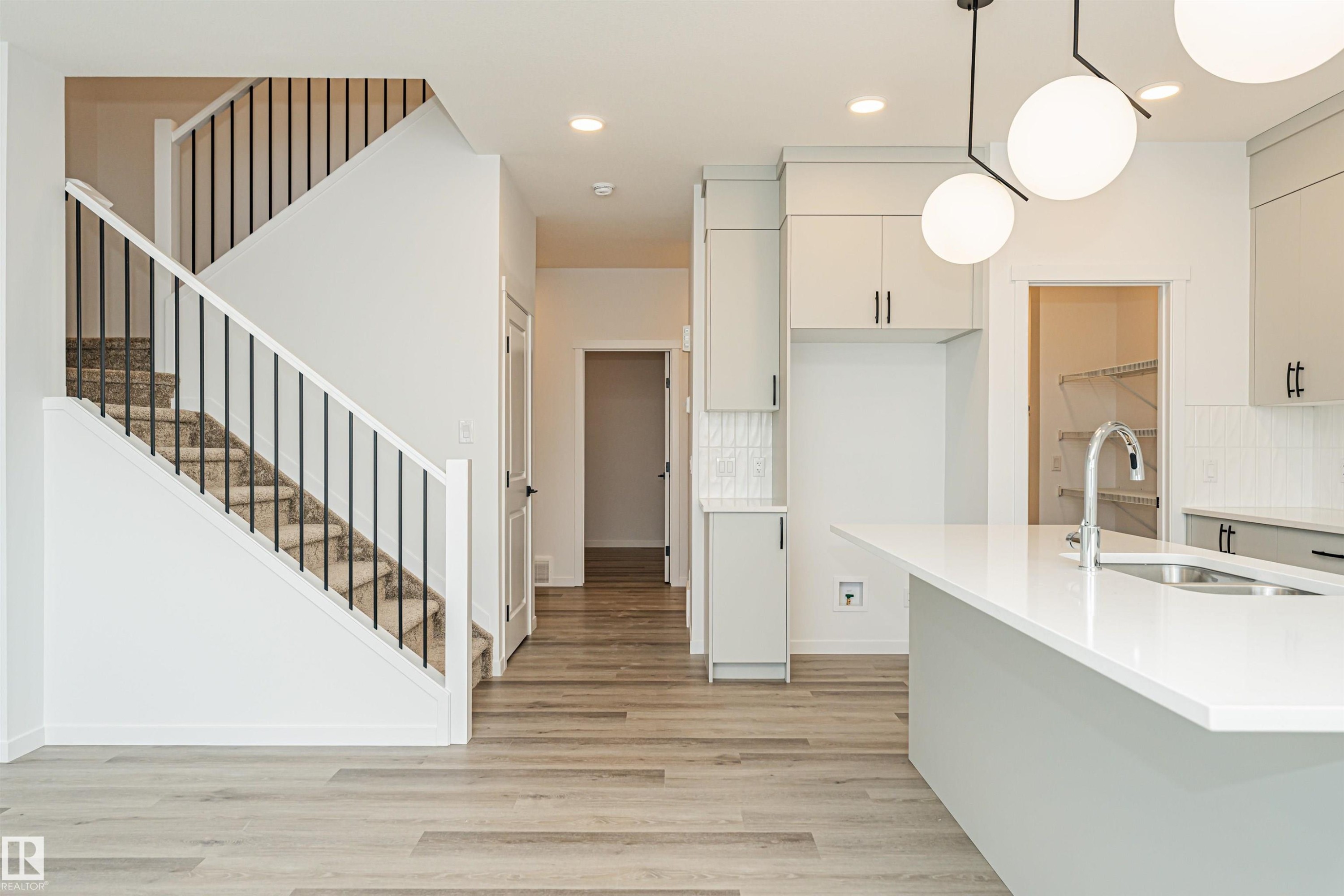 The property features a staircase with carpeted treads and black metal balusters, complemented by light wood-style flooring - 2355 Egret Way, Edmonton, AB - Indoor Photo Showing Kitchen With Double Sink