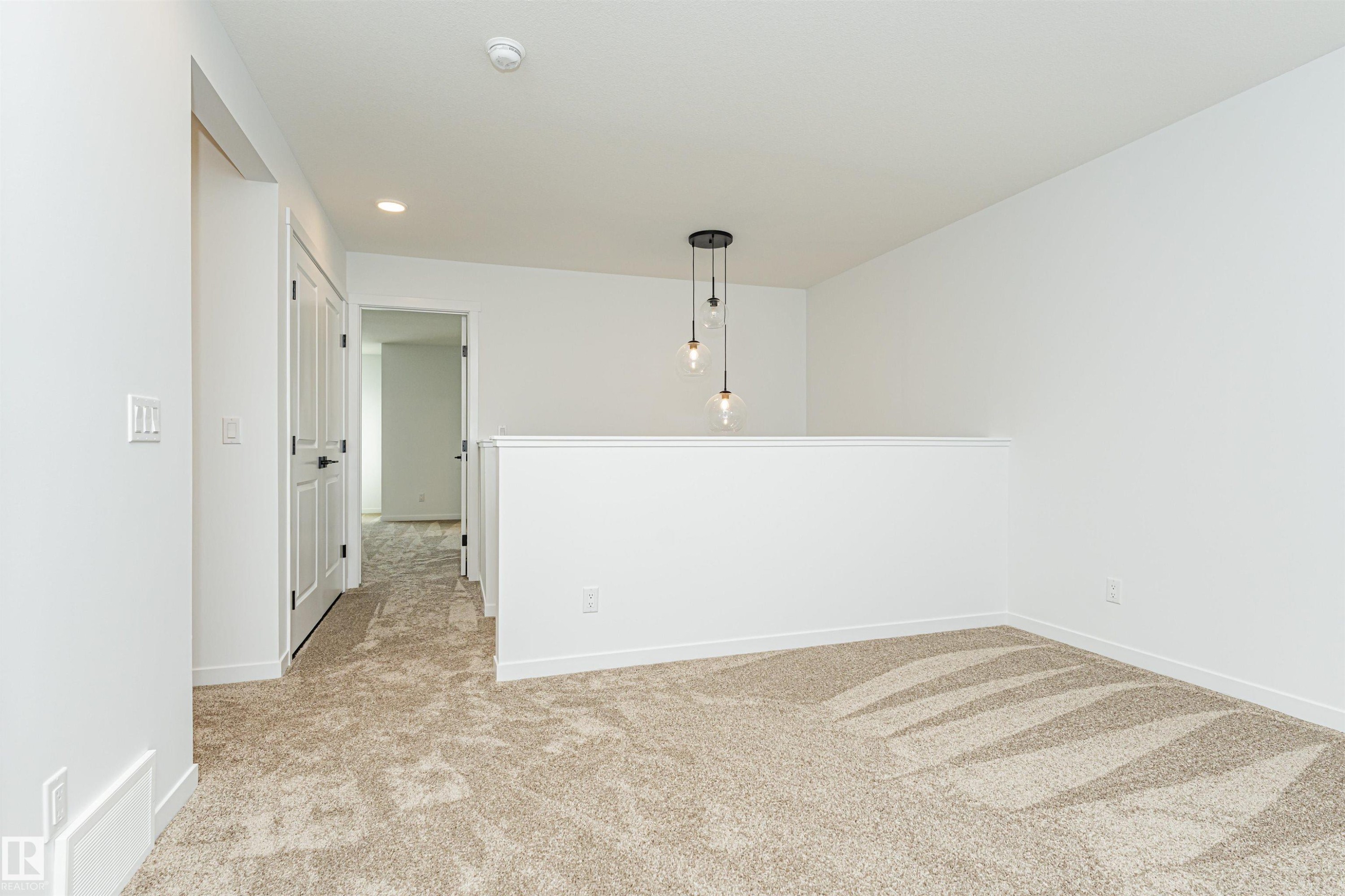 Open concept area featuring new carpet, white walls, and a contemporary hanging light fixture - 2355 Egret Way, Edmonton, AB - Indoor Photo Showing Other Room