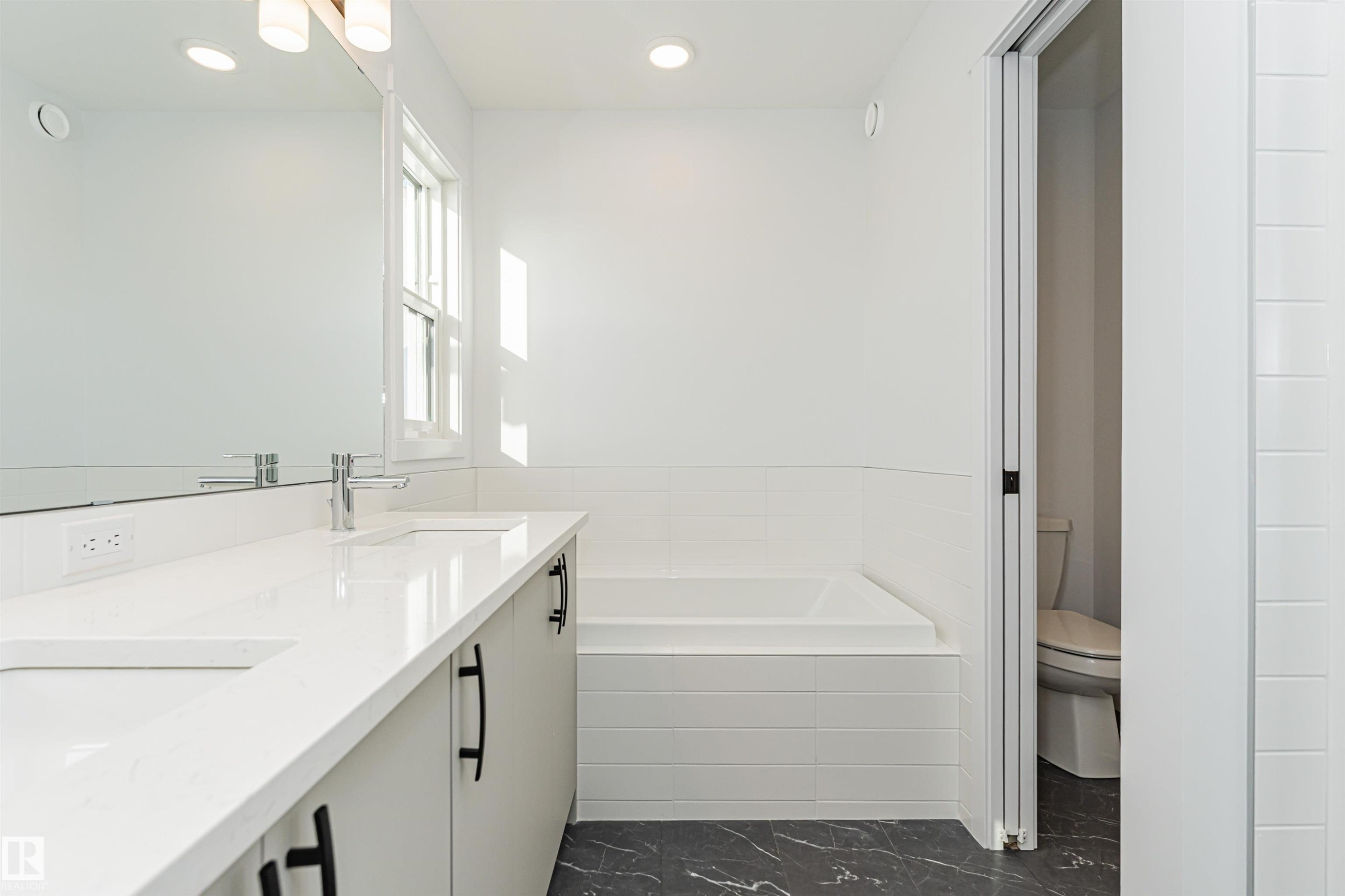 The bathroom features a double vanity with white countertops, a built-in bathtub, and dark patterned flooring - 2355 Egret Way, Edmonton, AB - Indoor Photo Showing Bathroom