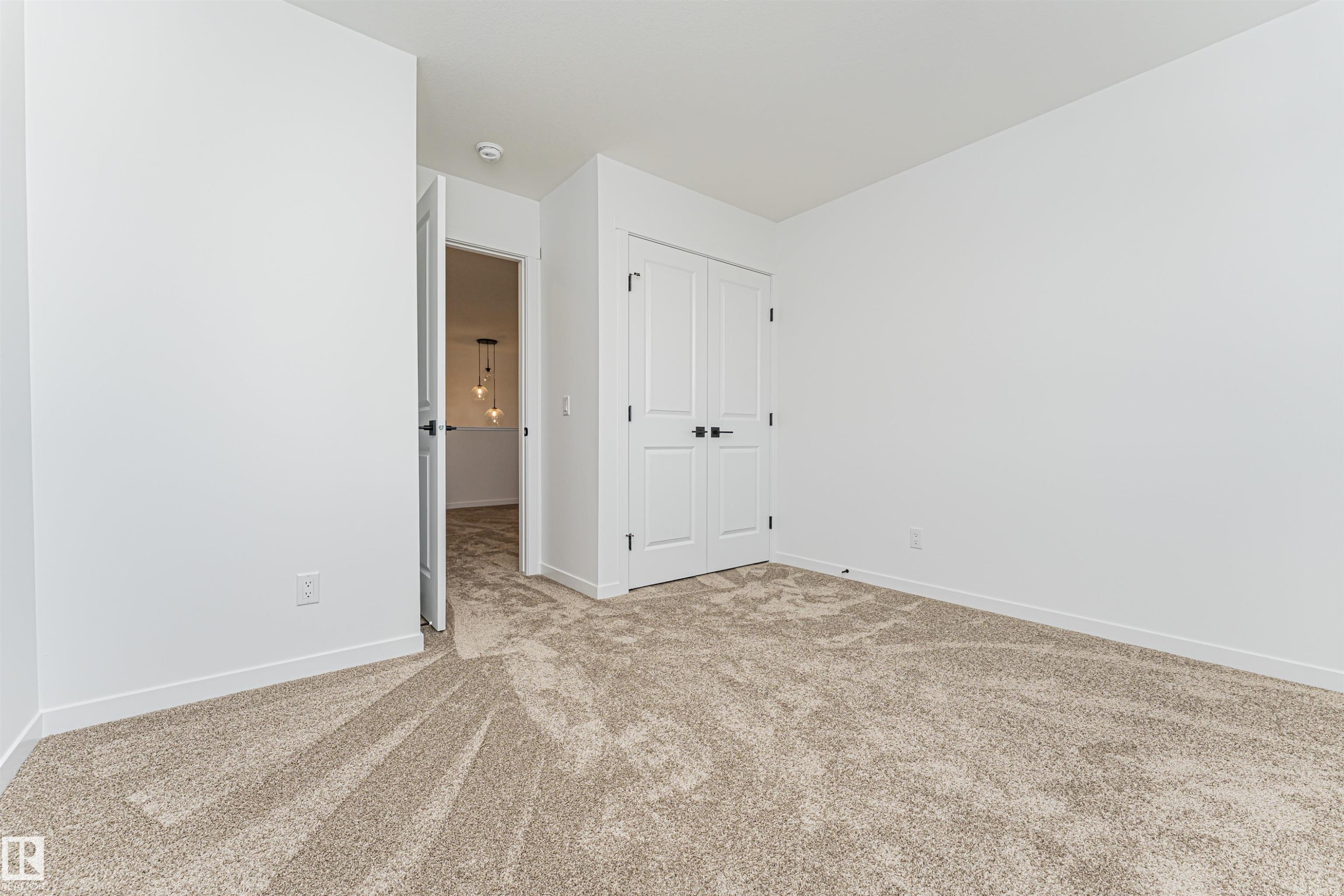 This room features plush carpet flooring, bright white walls, and white bi-fold closet doors with black hardware - 2355 Egret Way, Edmonton, AB - Indoor Photo Showing Other Room