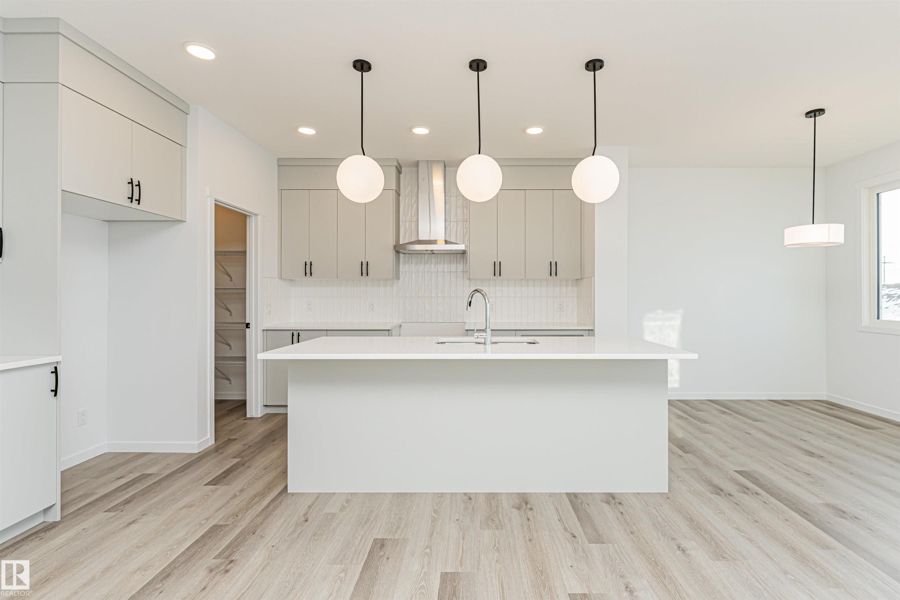 The kitchen features light-colored cabinetry, a white subway tile backsplash, and a large island with a sink and modern pendant lighting - 2355 Egret Way, Edmonton, AB - Indoor Photo Showing Kitchen With Upgraded Kitchen