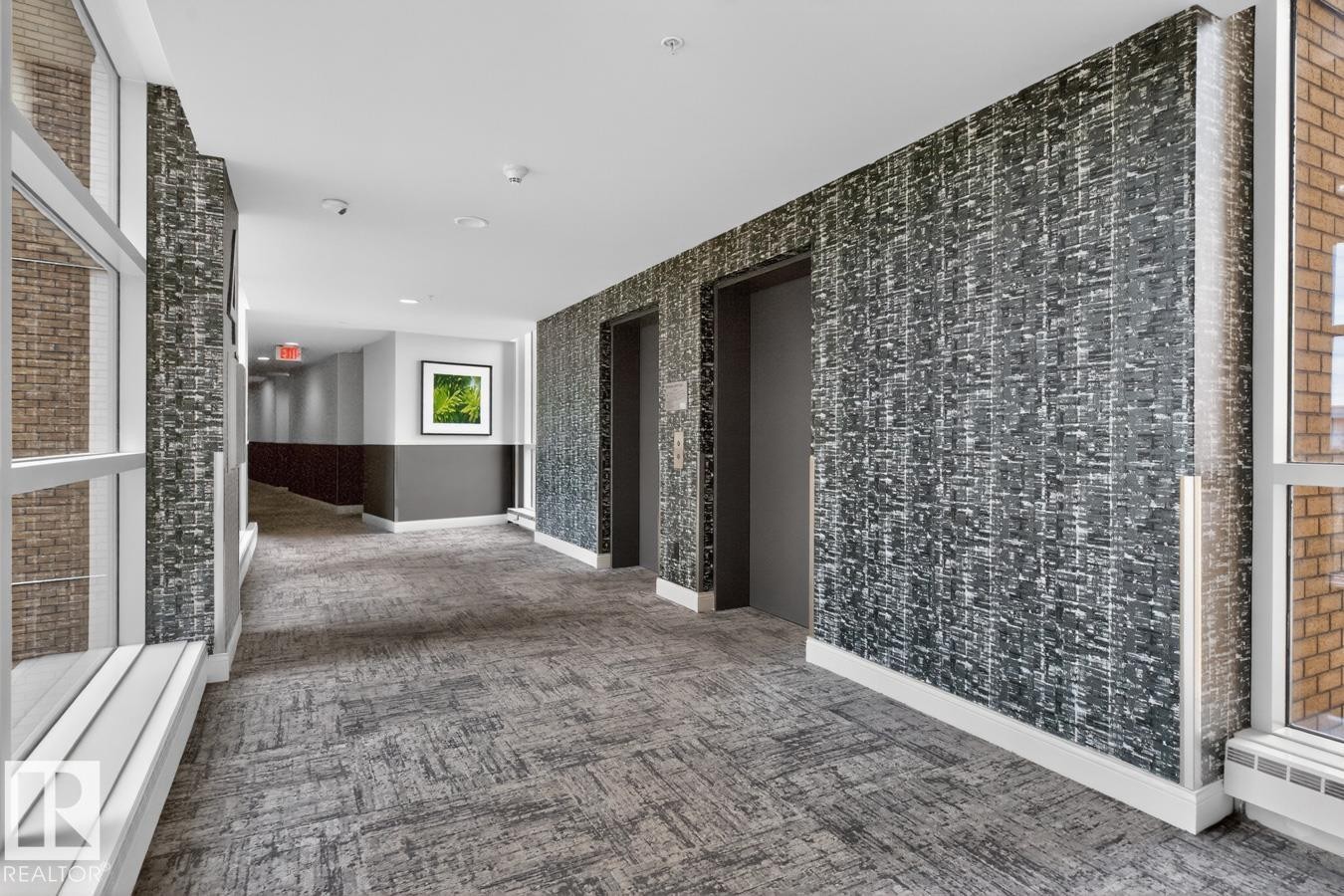 Hallway featuring patterned wall covering, two elevator doors, large windows, recessed lighting, and patterned carpet flooring - #407 2504 109 St Nw, Edmonton, AB - Indoor Photo Showing Other Room