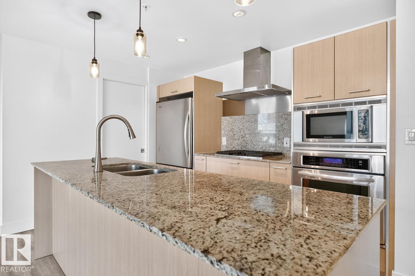 Spacious kitchen island featuring a dual-basin stainless steel sink with a gooseneck faucet, granite countertops, light wood-finish cabinetry, stainless steel appliances, and pendant lighting - #407 2504 109 St Nw, Edmonton, AB - Indoor Photo Showing Kitchen With Double Sink With Upgraded Kitchen