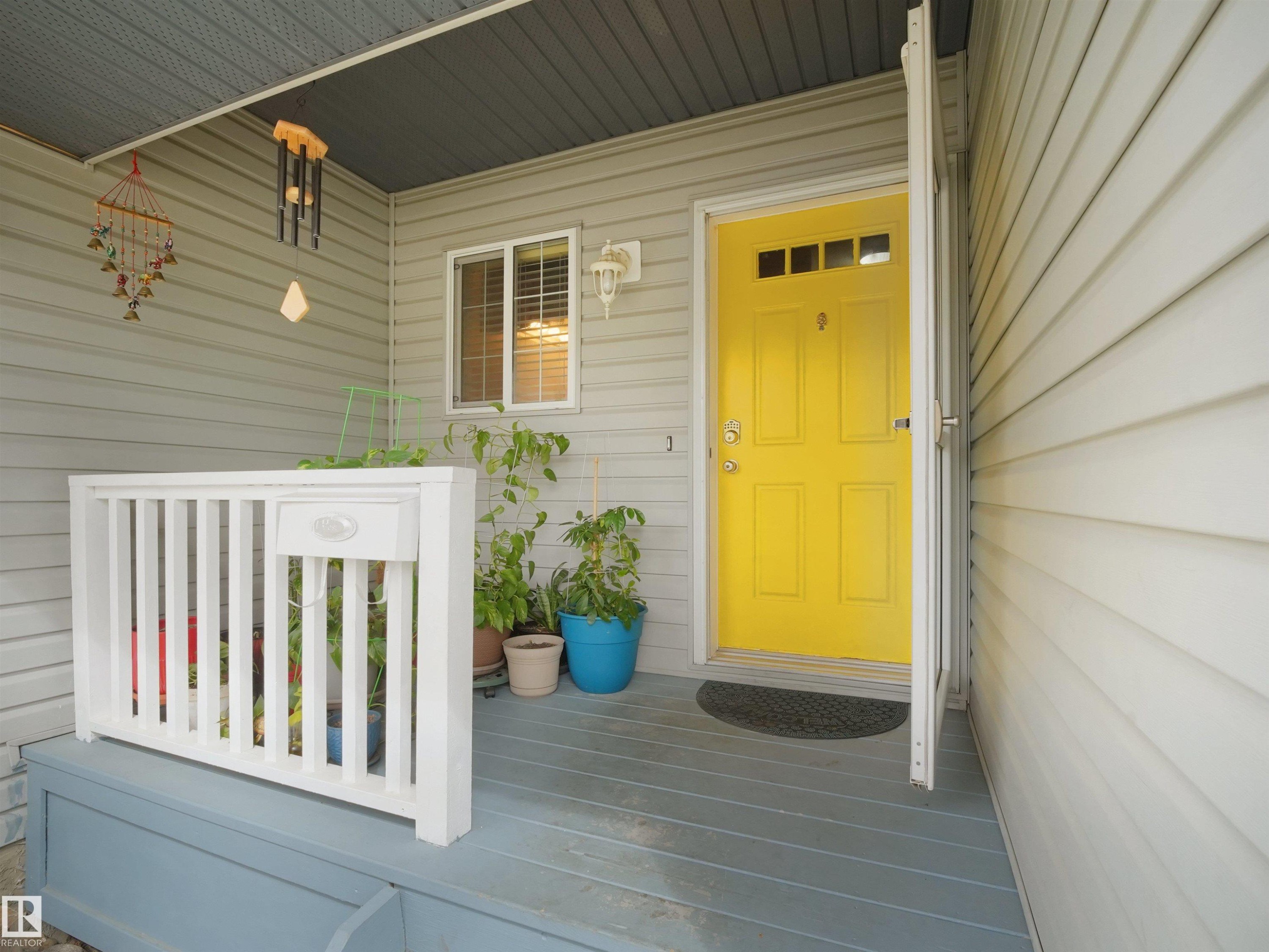 Welcoming front porch featuring a vibrant yellow entry door with upper lites, durable siding, and a painted wood deck - 16121 131A Street, Edmonton, AB - Outdoor With Exterior