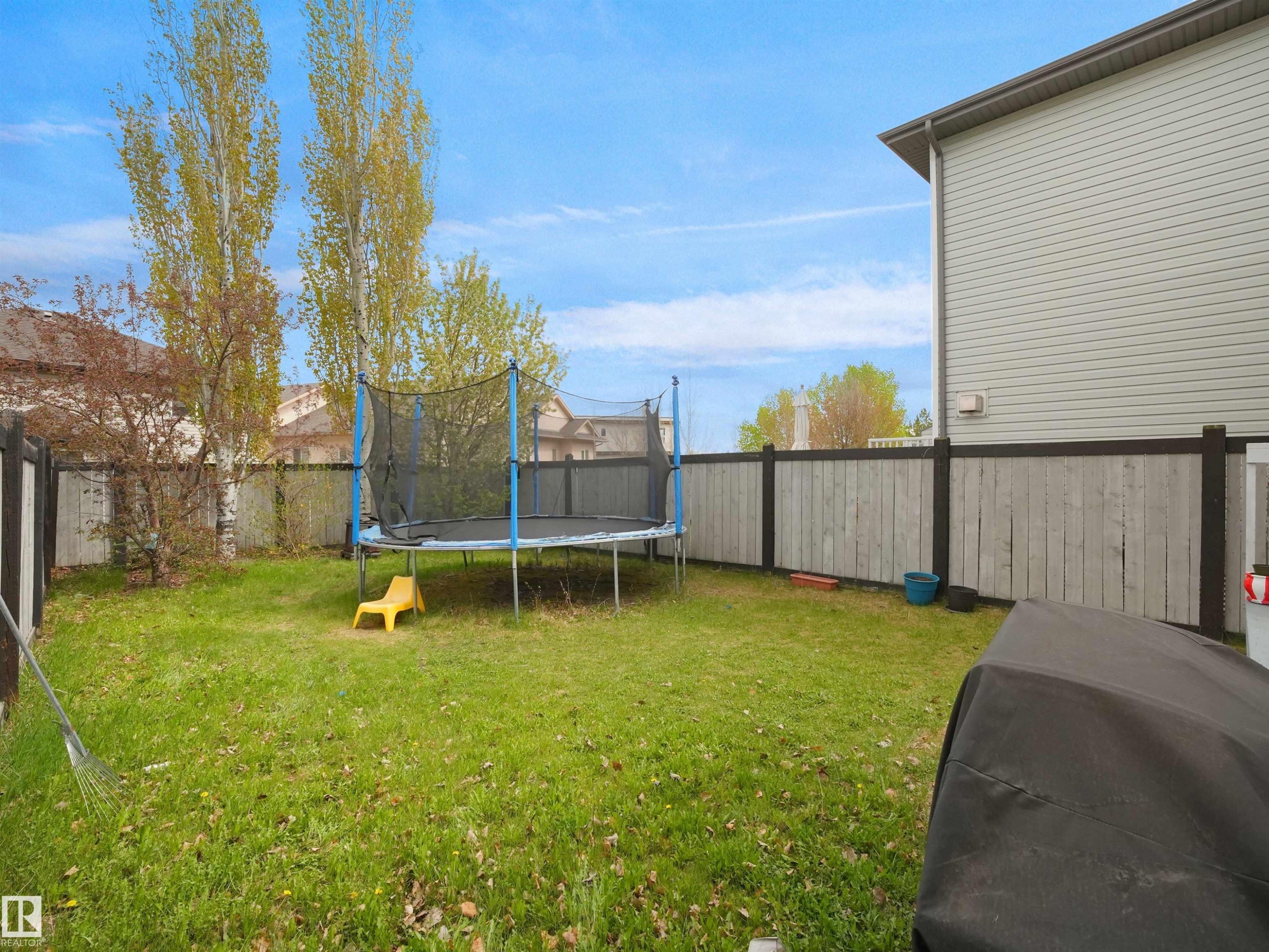 Expansive backyard featuring a green lawn, mature deciduous trees, and a full perimeter privacy fence with stained posts and light-toned panels - 16121 131A Street, Edmonton, AB - Outdoor