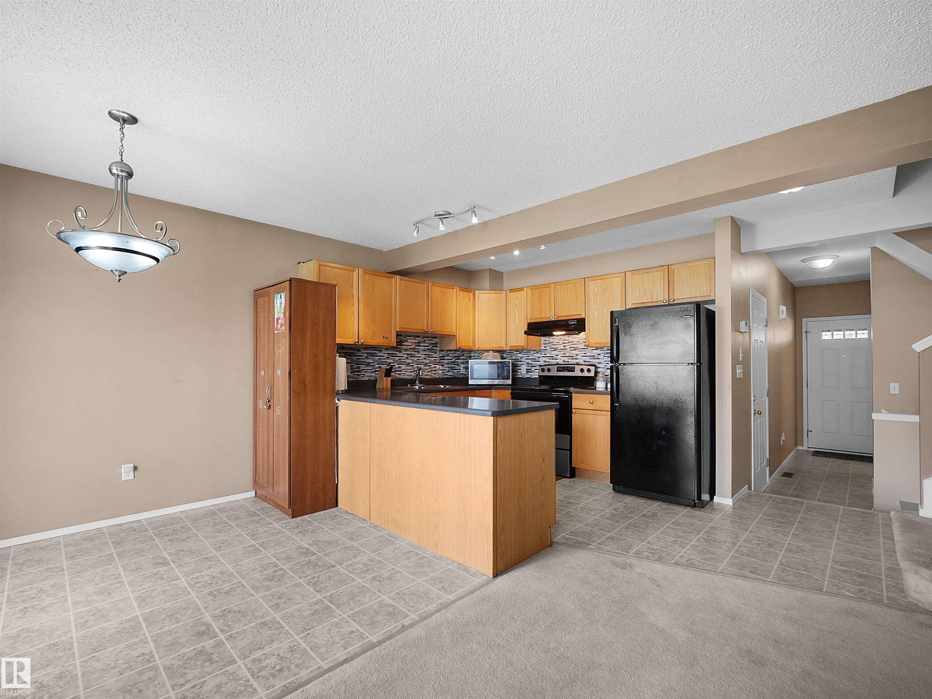 Open-concept kitchen and dining area featuring light wood cabinetry, dark countertops, a dark tile backsplash, and a central island - 16121 131A Street, Edmonton, AB - Indoor Photo Showing Kitchen