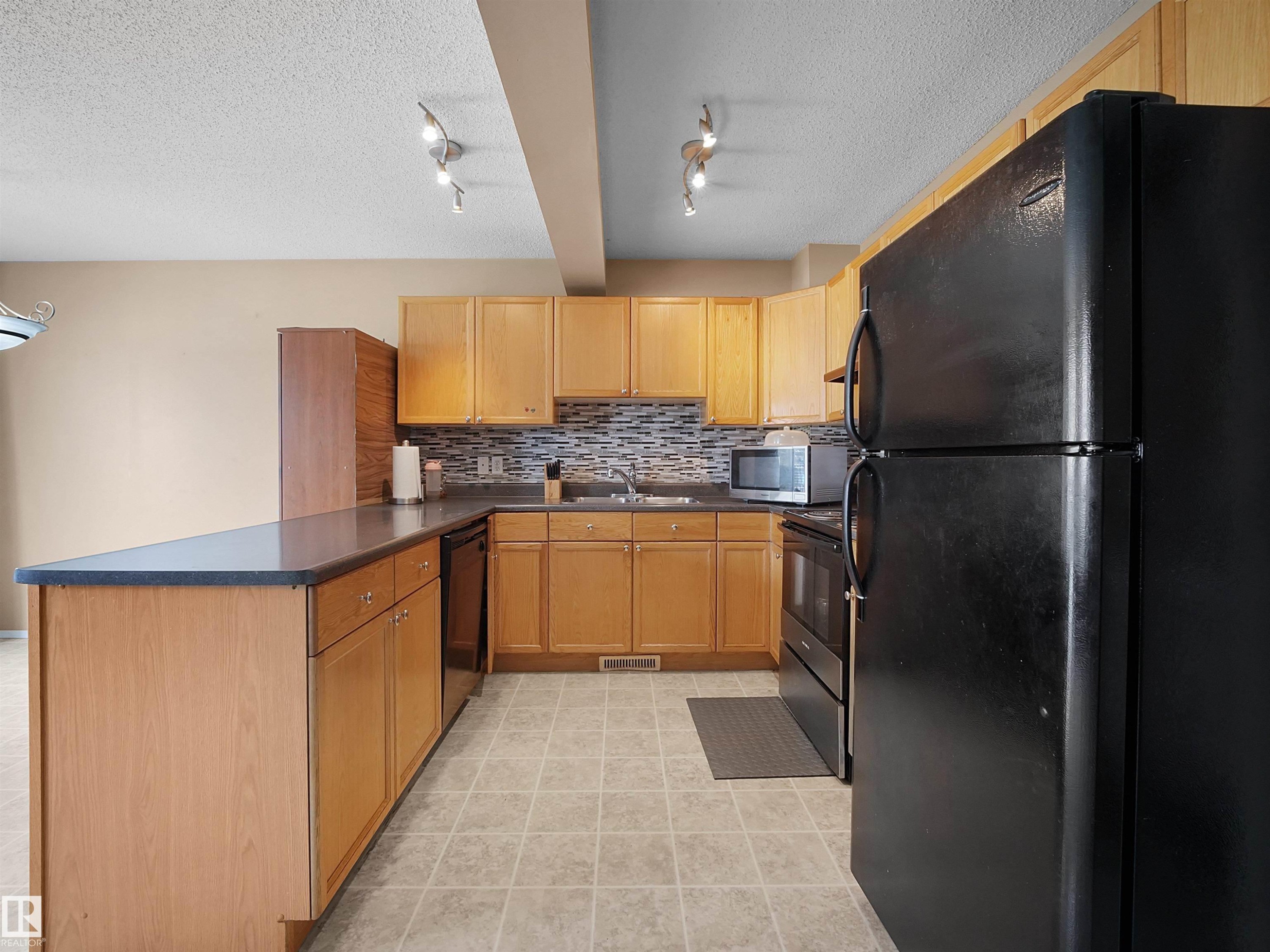 Kitchen featuring natural wood cabinetry, a dark countertop, and a mosaic tile backsplash - 16121 131A Street, Edmonton, AB - Indoor Photo Showing Kitchen