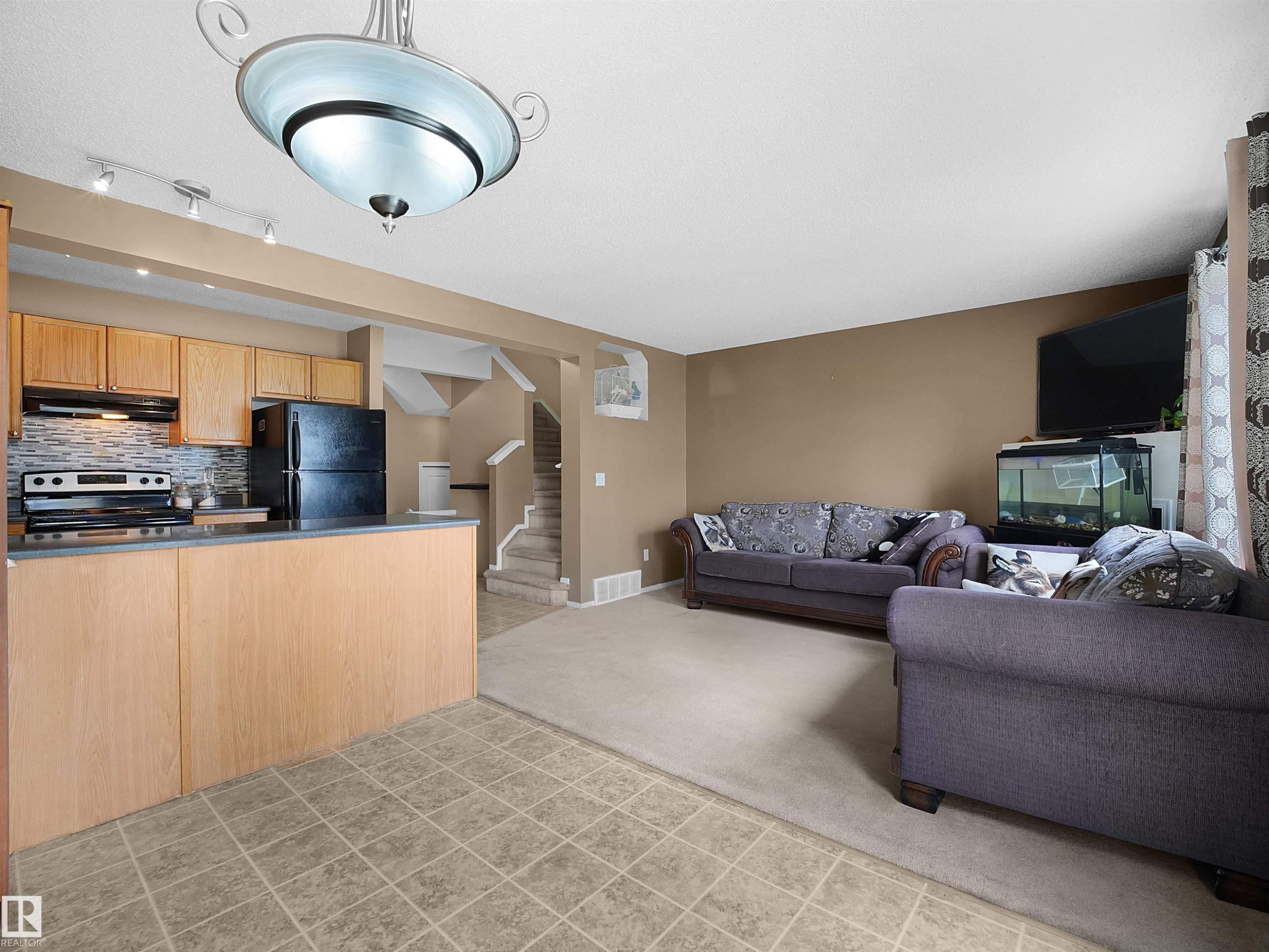 Open concept living area featuring a kitchen with light wood cabinetry, a mosaic tile backsplash, and a breakfast bar - 16121 131A Street, Edmonton, AB - Indoor Photo Showing Kitchen