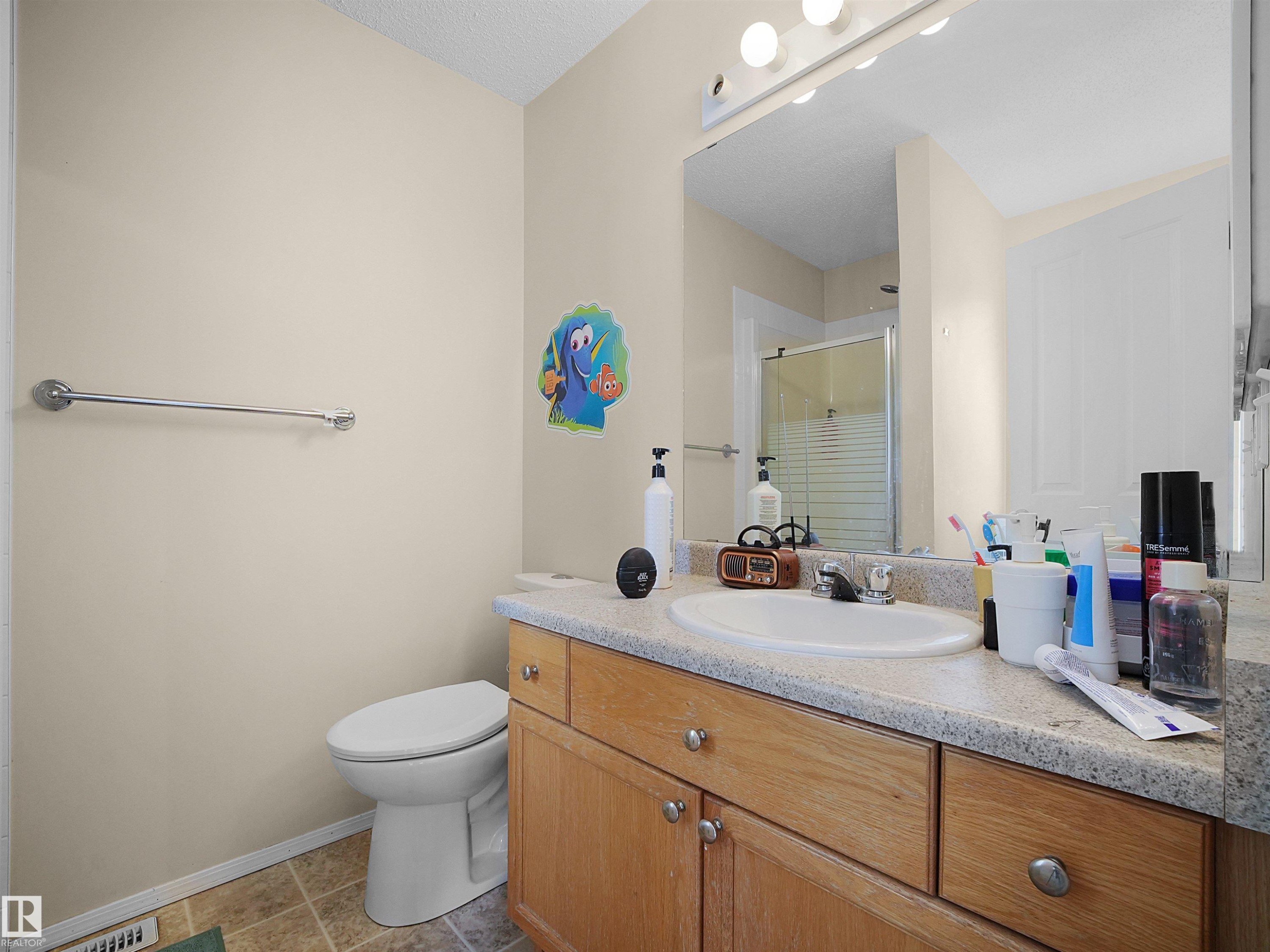 Bathroom featuring a wood-finish vanity with an integrated sink and light-toned countertop, a wall-mounted mirror with overhead lighting, and a walk-in shower with a glass enclosure - 16121 131A Street, Edmonton, AB - Indoor Photo Showing Bathroom