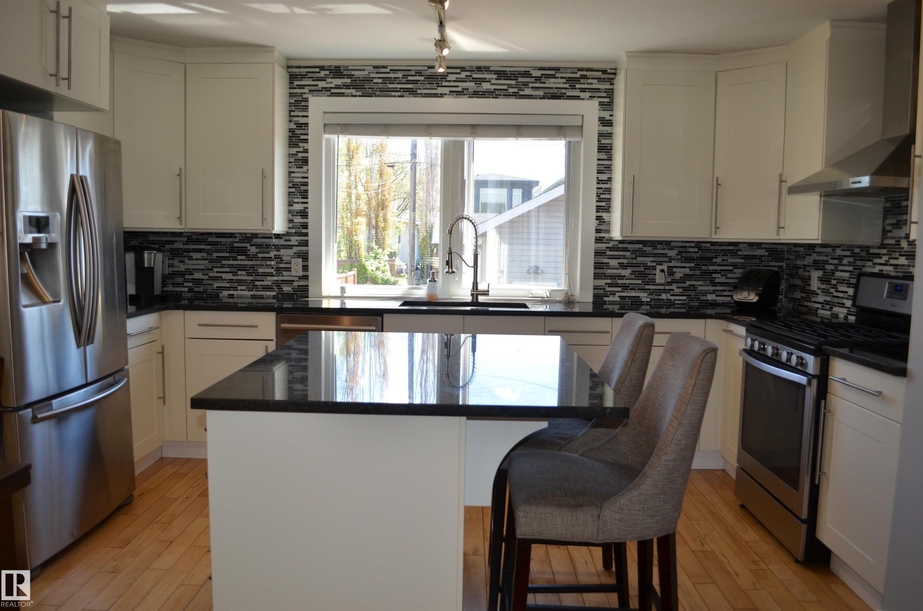 Kitchen featuring an island with a dark countertop, stainless steel appliances, white cabinetry, and a mosaic tile backsplash - 10527 81 Street, Edmonton, AB - Indoor Photo Showing Kitchen With Upgraded Kitchen