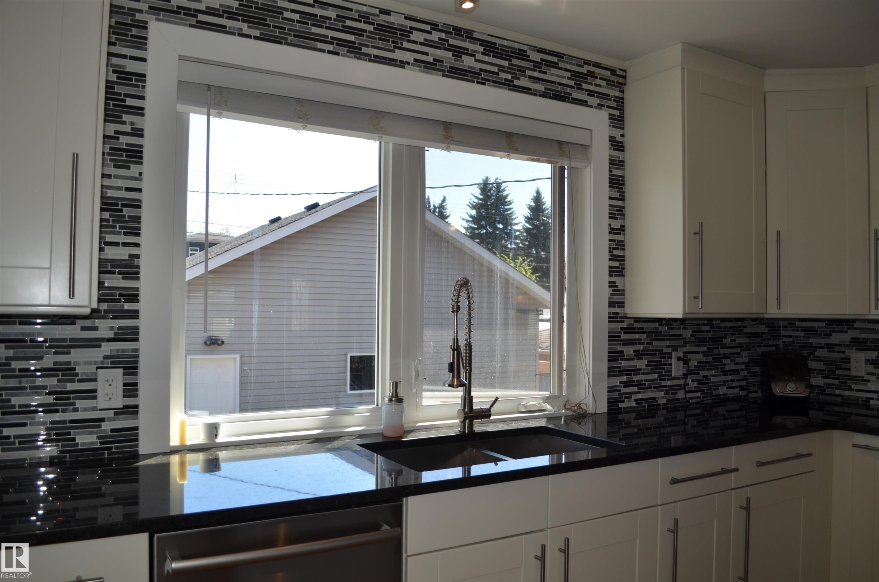 Kitchen featuring white shaker-style cabinetry with brushed nickel hardware, black stone countertops, a mosaic tile backsplash, and a double-basin sink with a gooseneck faucet - 10527 81 Street, Edmonton, AB - Indoor Photo Showing Kitchen With Double Sink