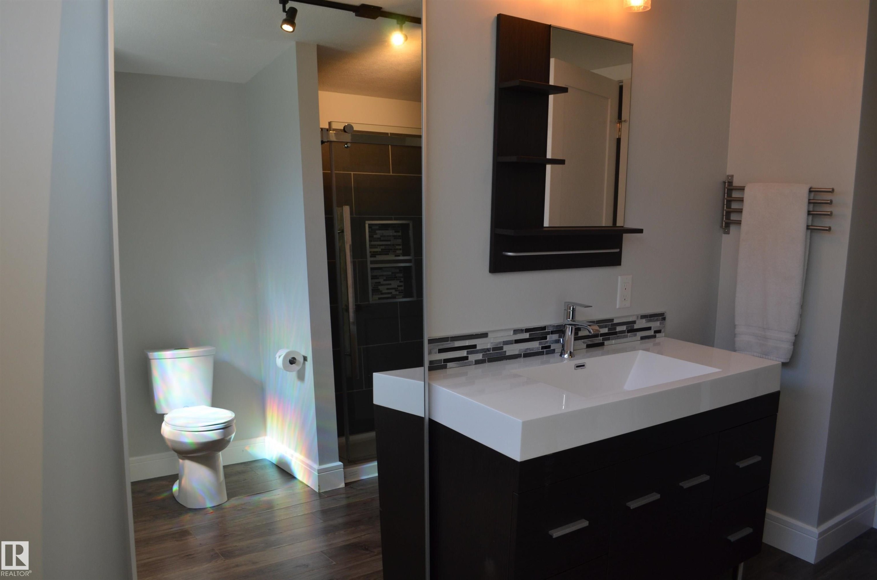 Modern vanity with an integrated white sink, chrome faucet, and a mosaic tile backsplash - 10527 81 Street, Edmonton, AB - Indoor Photo Showing Bathroom