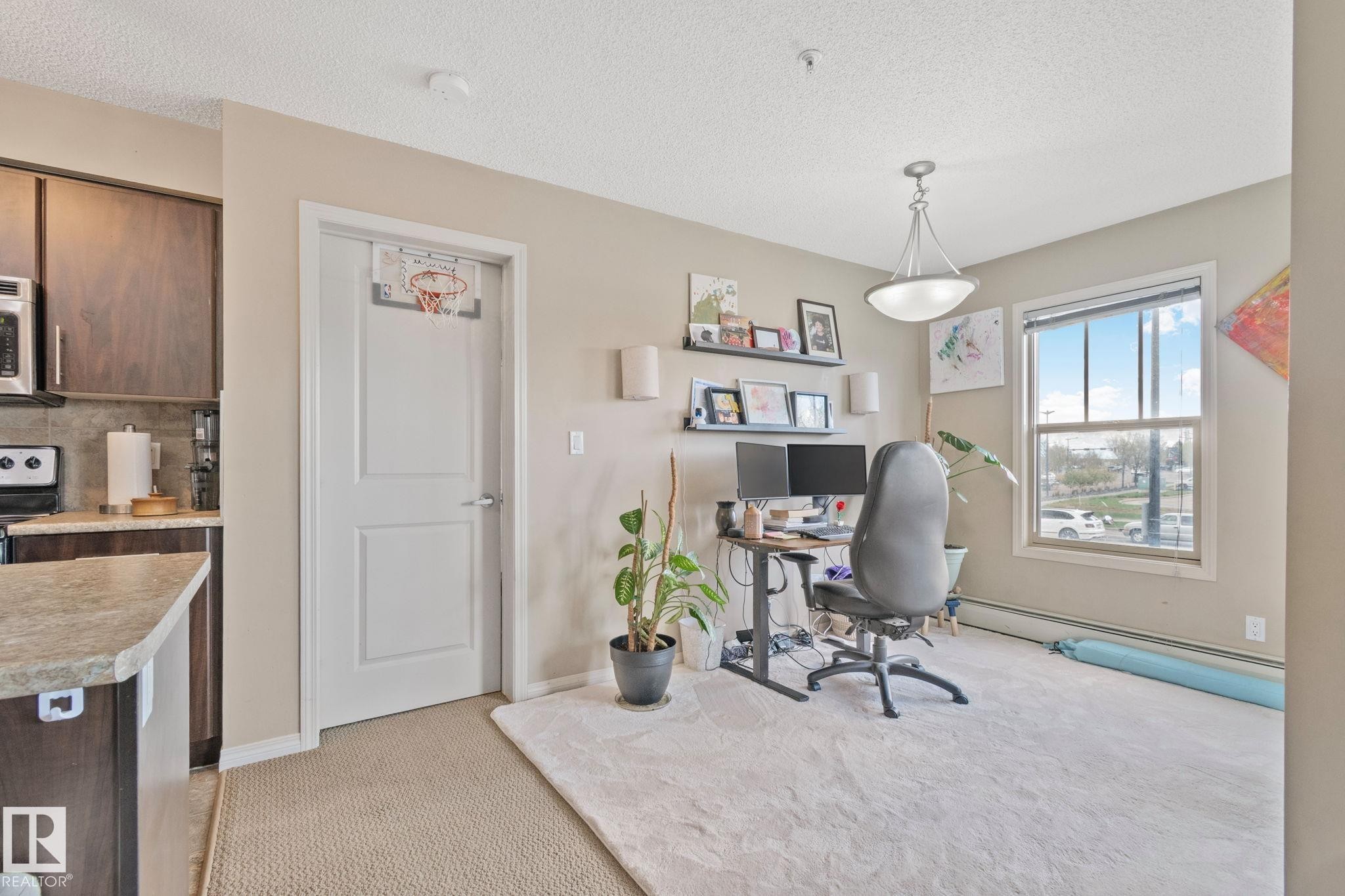 Versatile living area featuring a large window, pendant lighting, and neutral wall tones - 206 103 Ambleside Drive, Edmonton, AB - Indoor