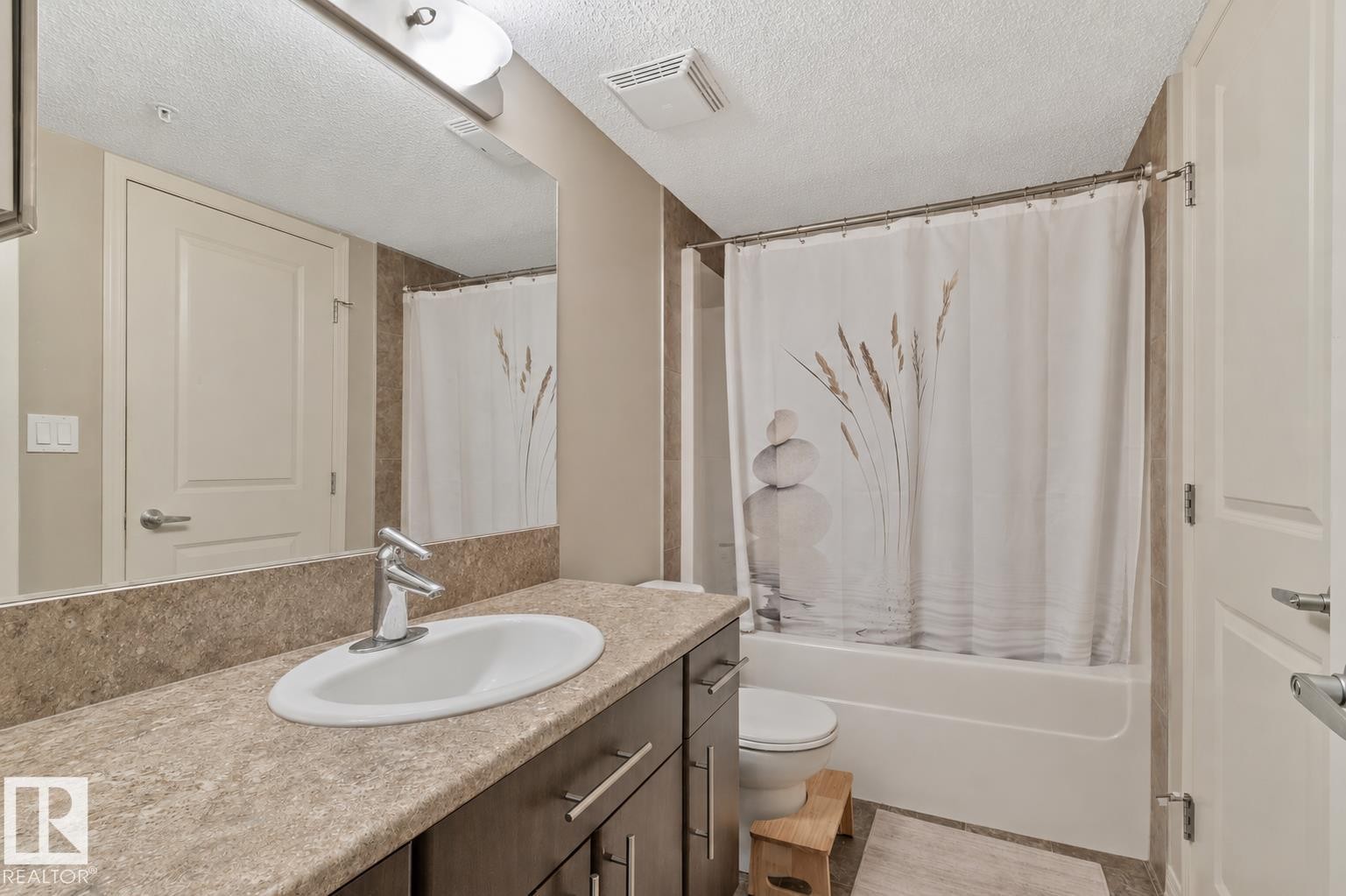 Bathroom featuring a wood-finish vanity with an integrated sink, stone-look countertop, and chrome faucet - 206 103 Ambleside Drive, Edmonton, AB - Indoor Photo Showing Bathroom