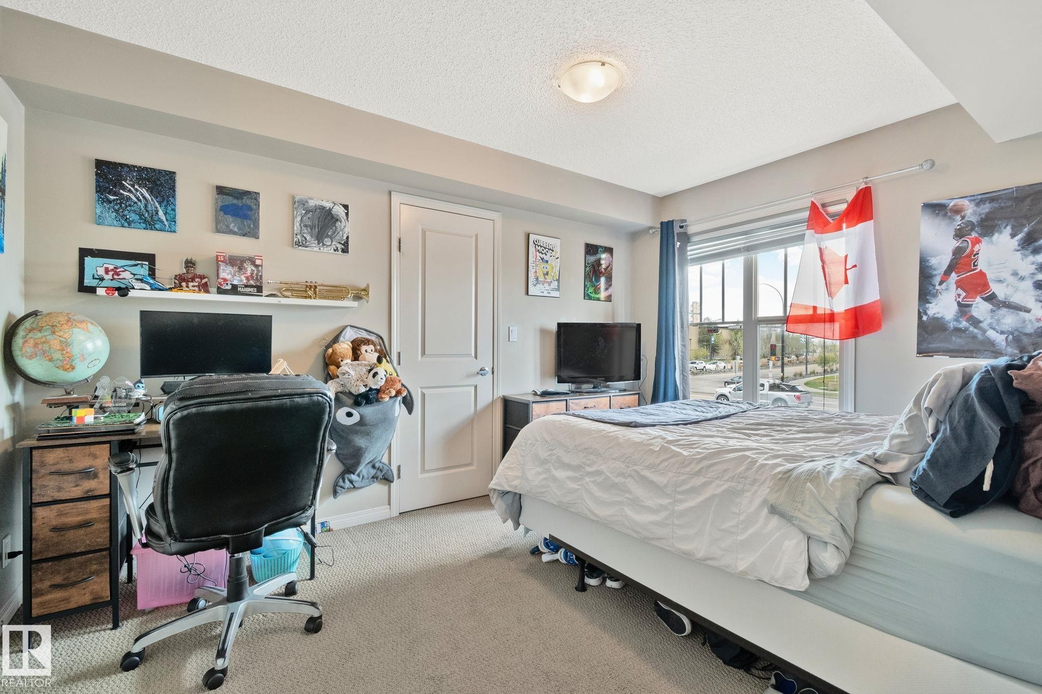 Bedroom featuring carpet flooring, a large window with horizontal blinds, a neutral wall color, a built-in overhead light fixture, and a white interior door - 206 103 Ambleside Drive, Edmonton, AB - Indoor
