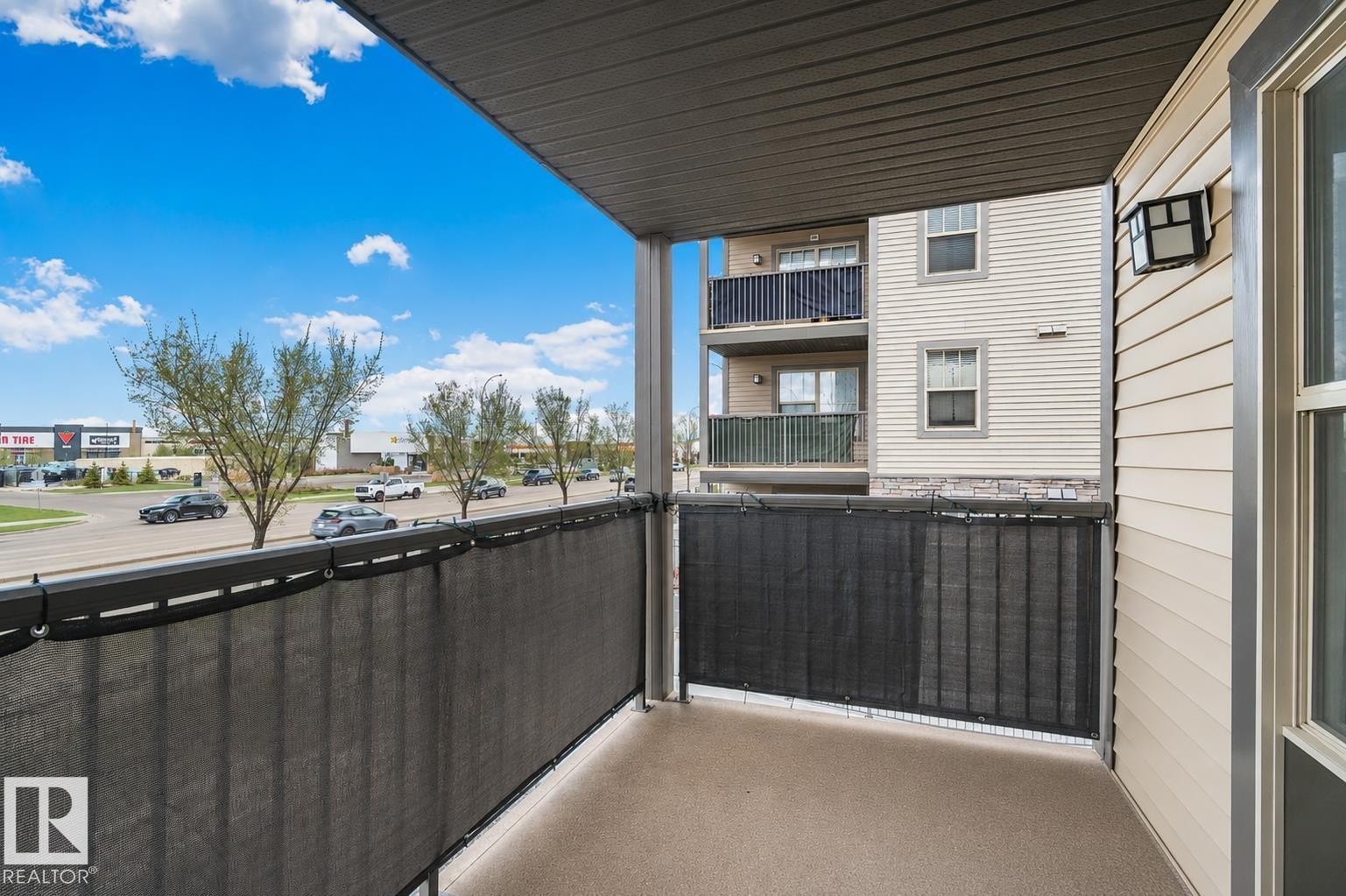 Outdoor balcony featuring a textured concrete floor, dark privacy screening, and an exterior wall light fixture - 206 103 Ambleside Drive, Edmonton, AB - Outdoor With Balcony With Exterior