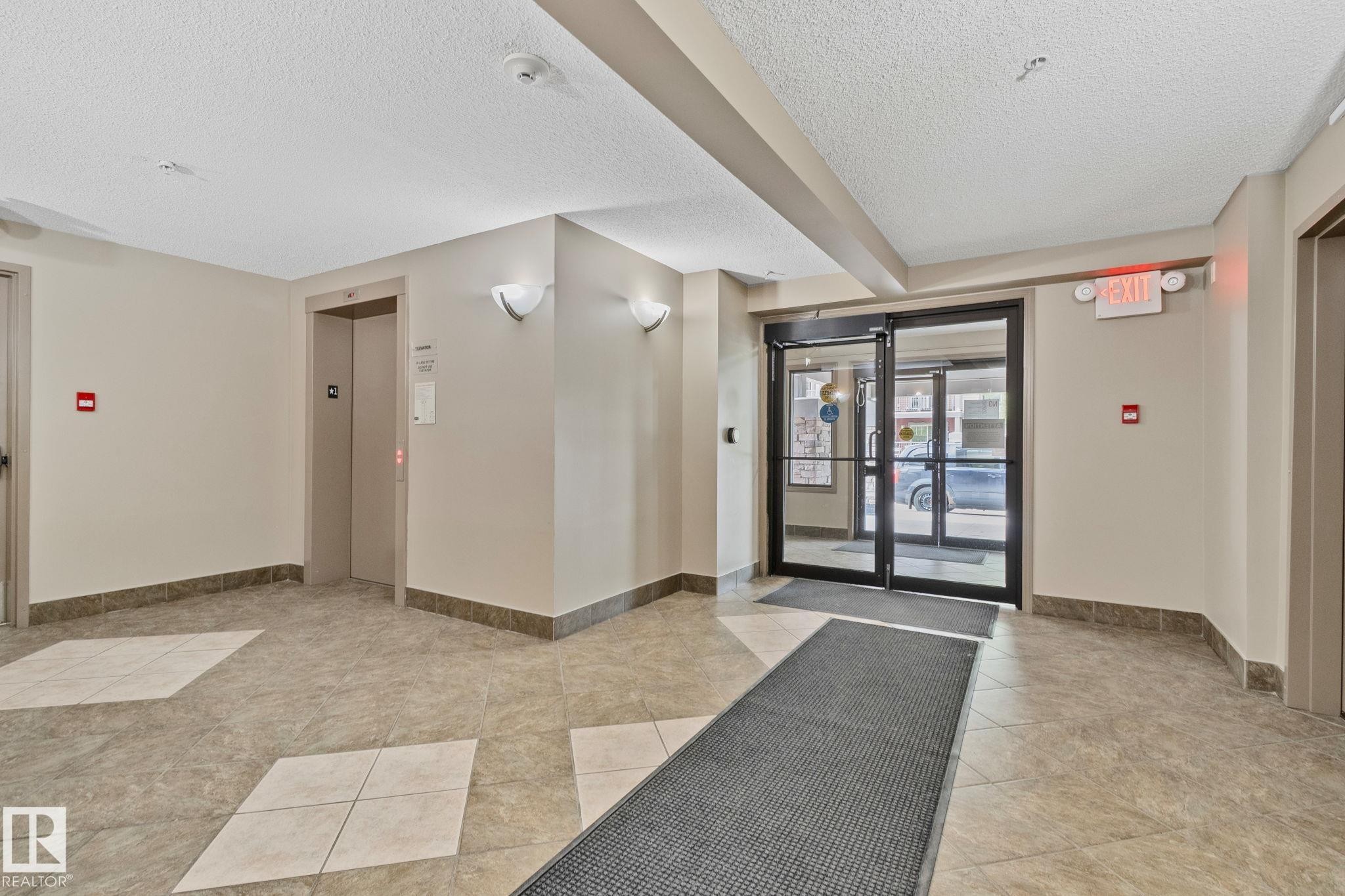 Building entrance lobby featuring tile flooring, glass entry doors, and wall sconces - 206 103 Ambleside Drive, Edmonton, AB - Indoor Photo Showing Other Room