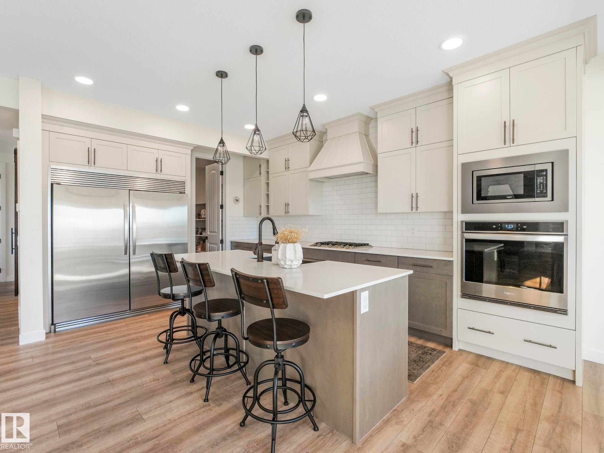 Gourmet kitchen featuring a large central island with seating, stainless steel appliances, white subway tile backsplash, light wood-finish flooring, and recessed lighting - 6613 62 Avenue, Beaumont, AB - Indoor Photo Showing Kitchen With Upgraded Kitchen