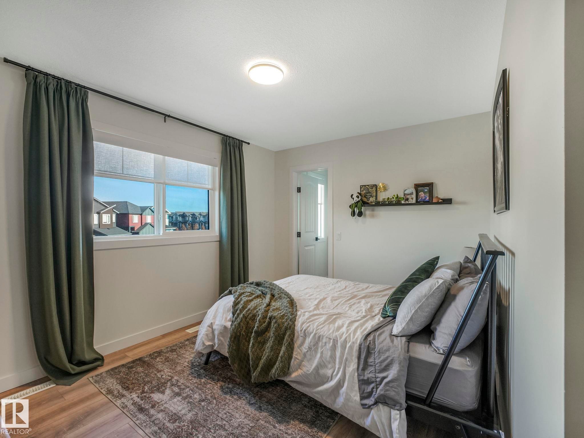 Spacious room featuring wood-finish flooring, a contemporary ceiling light fixture, and a window with blinds - 6613 62 Avenue, Beaumont, AB - Indoor Photo Showing Bedroom