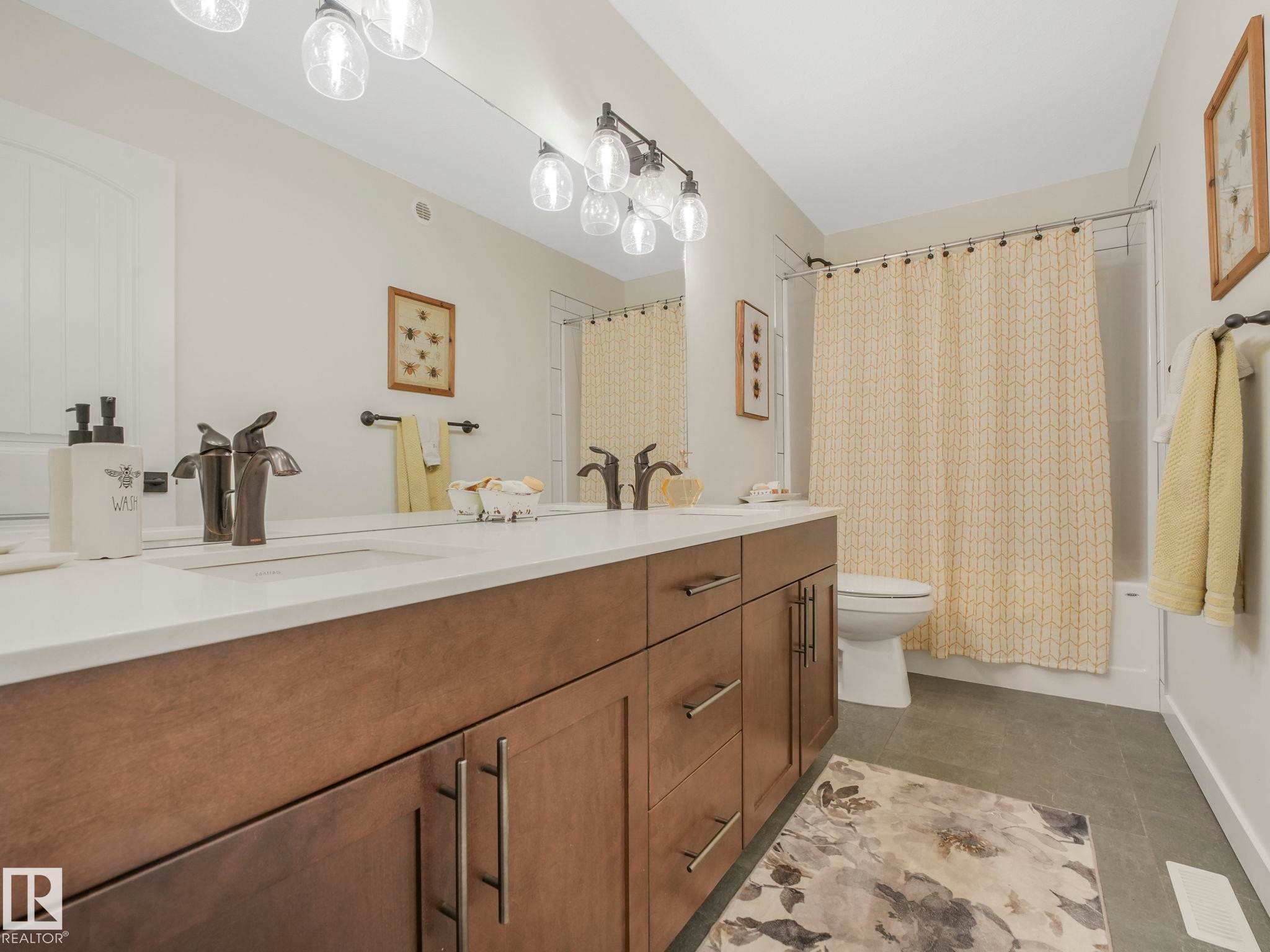 Double vanity with a white countertop and dark wood-finish cabinetry, featuring dual undermount sinks and dark bronze-finish faucets - 6613 62 Avenue, Beaumont, AB - Indoor Photo Showing Bathroom