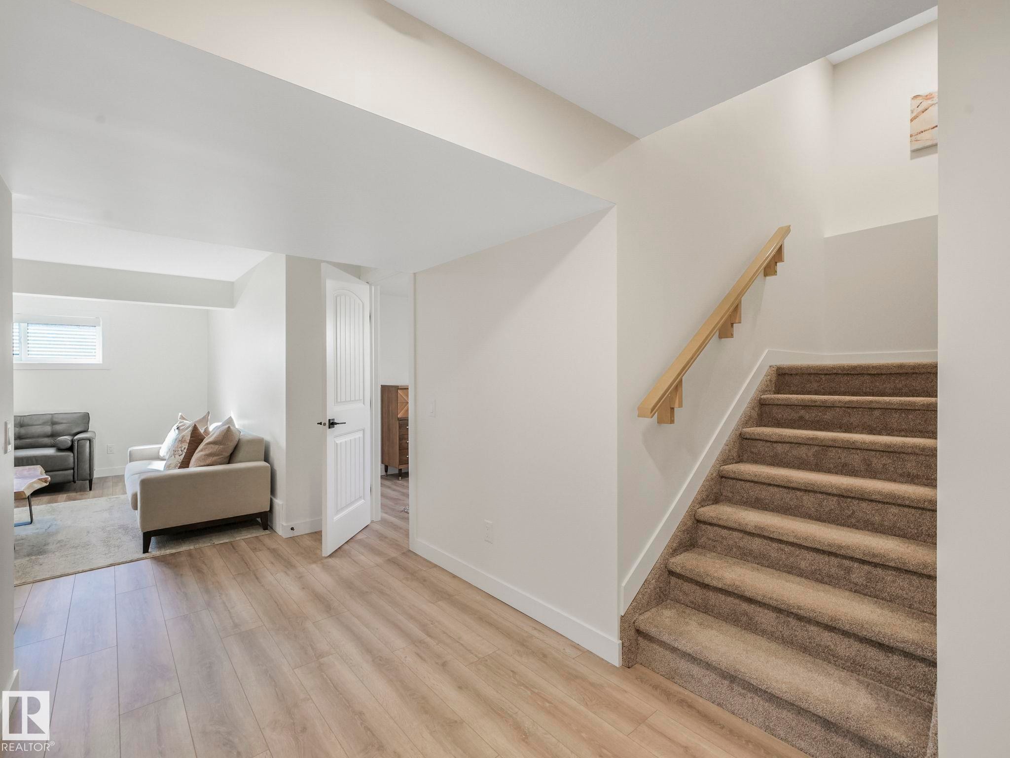 Finished basement space featuring wood-finish flooring, a carpeted staircase with a wood handrail, and white walls - 6613 62 Avenue, Beaumont, AB - Indoor Photo Showing Other Room