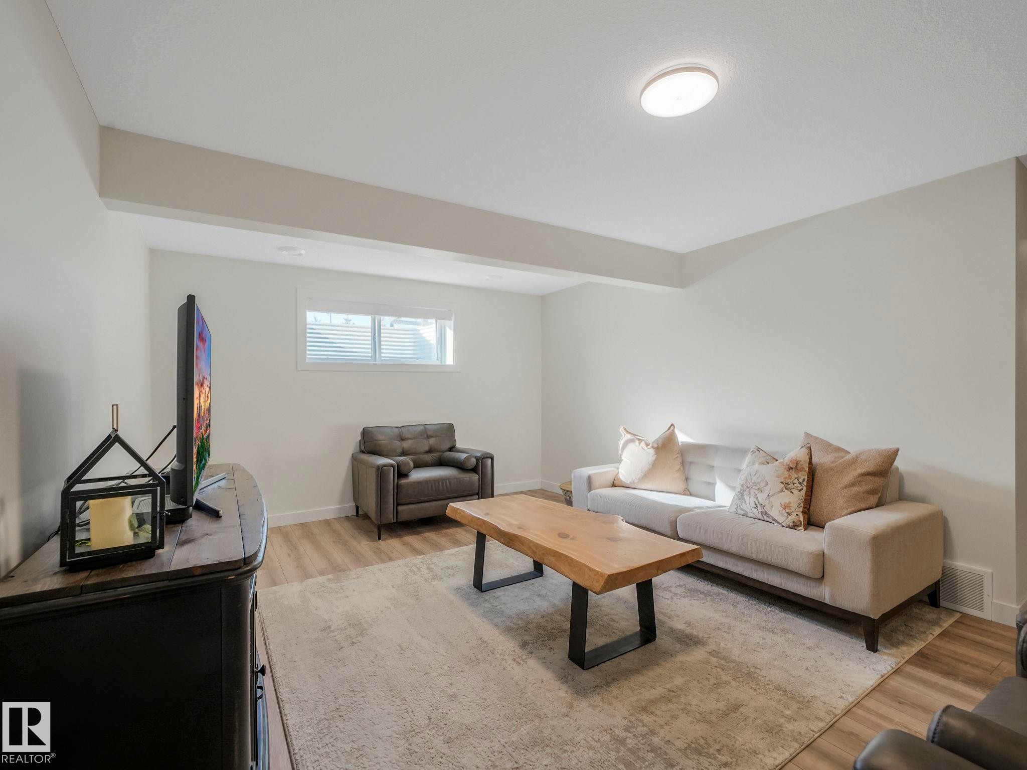 Spacious living area featuring wood-finish flooring, a neutral color palette, recessed window with blinds, and ceiling-mounted lighting - 6613 62 Avenue, Beaumont, AB - Indoor