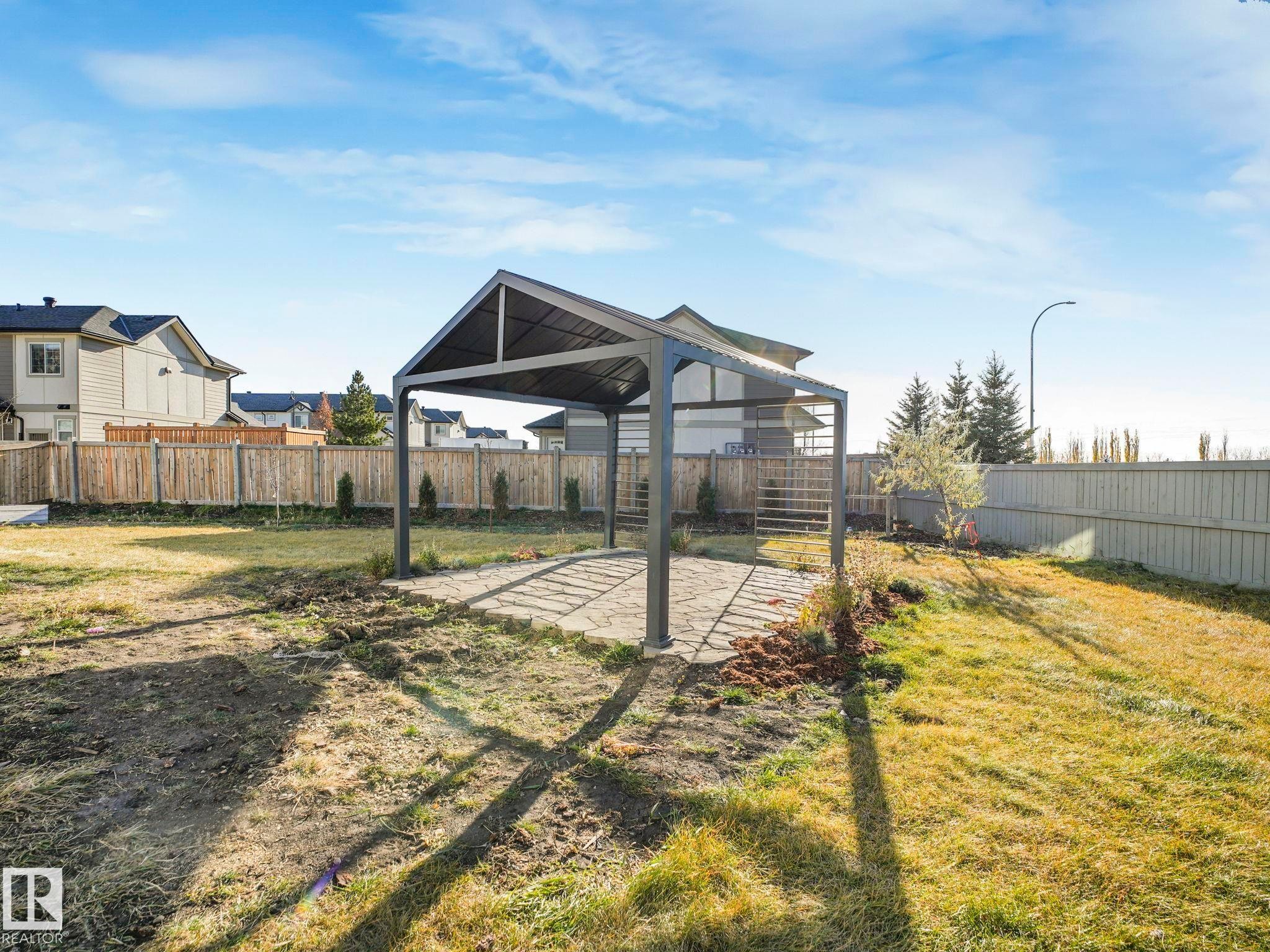 Spacious backyard featuring a metal pergola with a paved stone base, a wooden perimeter fence, and young trees - 6613 62 Avenue, Beaumont, AB - Outdoor