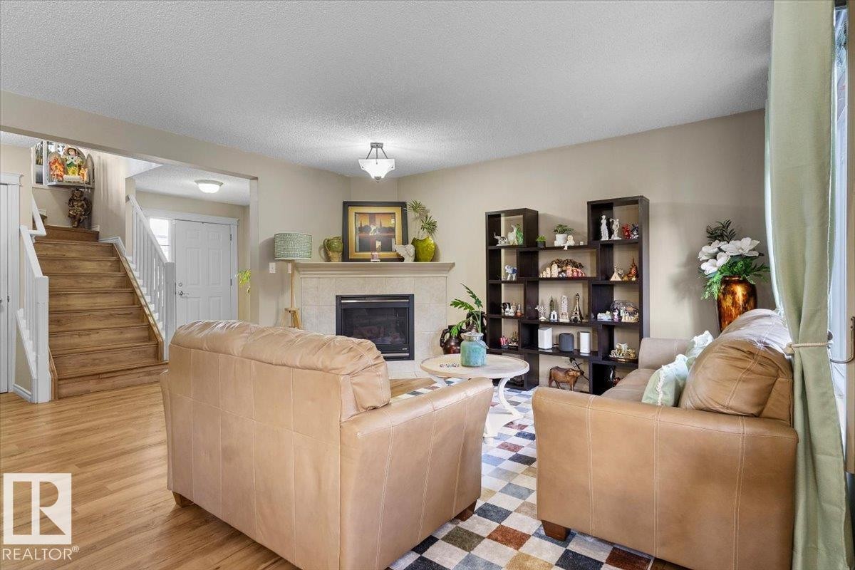 Living area featuring a fireplace with a light-toned mantel, wood-finish flooring, and a white paneled entry door - 3356 25 Ave, Edmonton, AB - Indoor Photo Showing Living Room With Fireplace