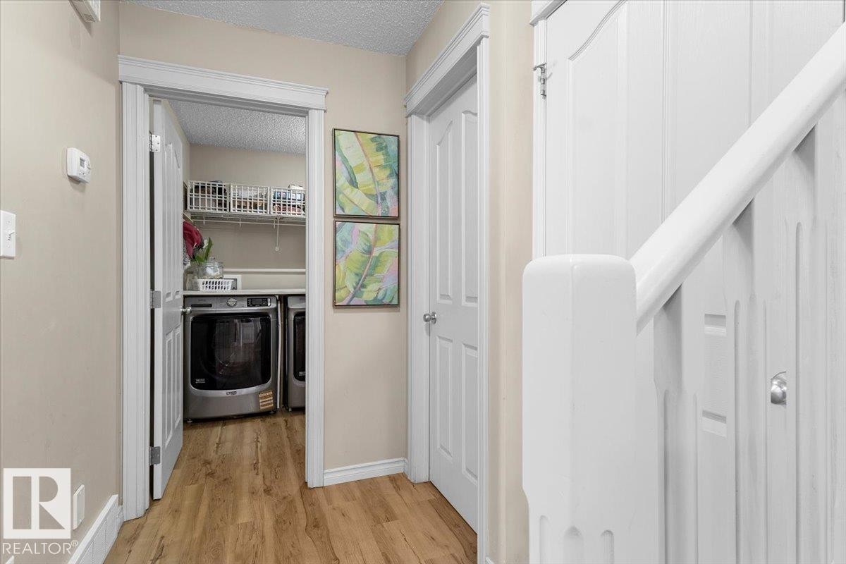 Dedicated laundry area featuring a washer and dryer, wire shelving, and wood-finish flooring - 3356 25 Ave, Edmonton, AB - Indoor